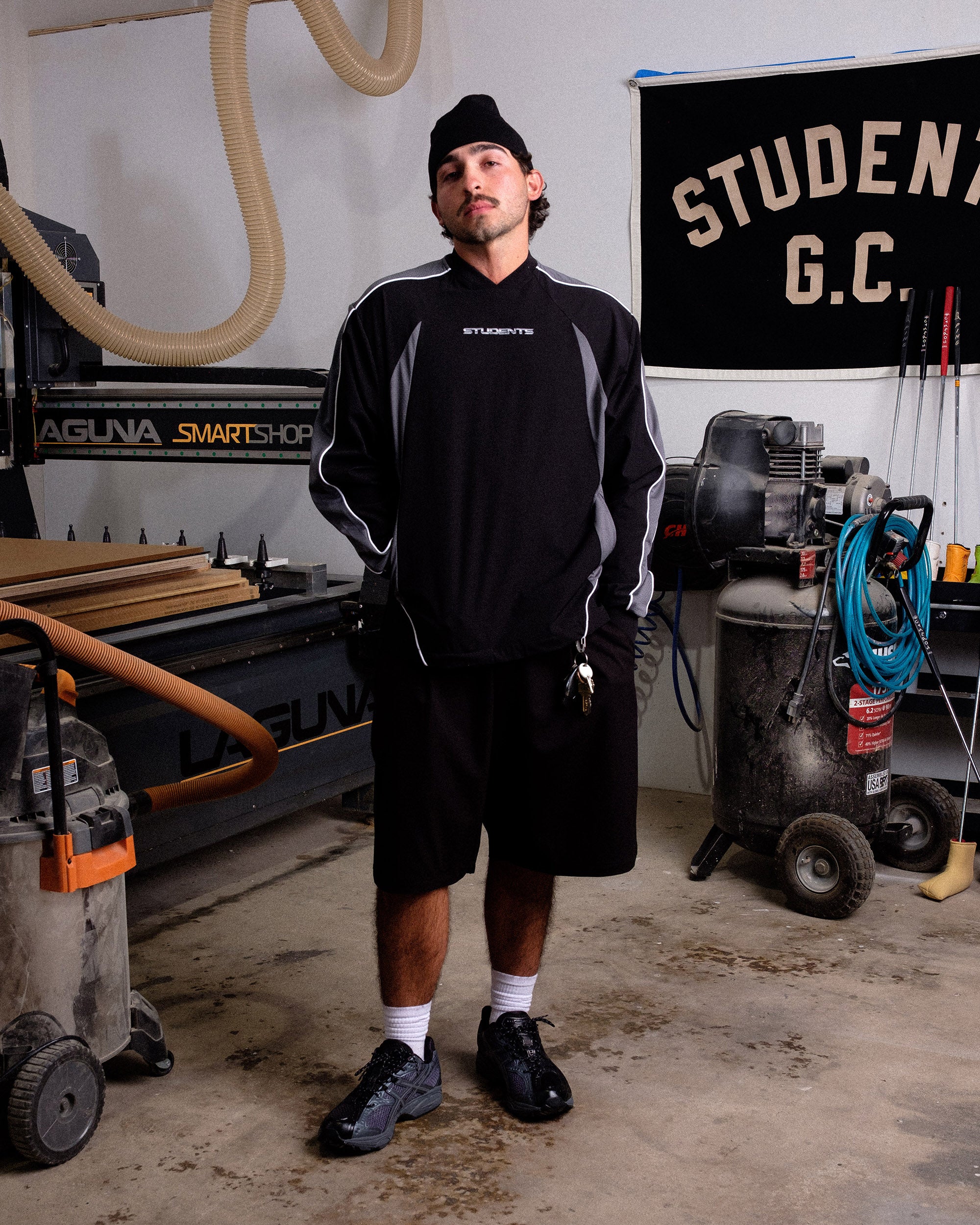 Man standing in a workshop wearing a black and gray sweatshirt with 'STUDENT' branding.
