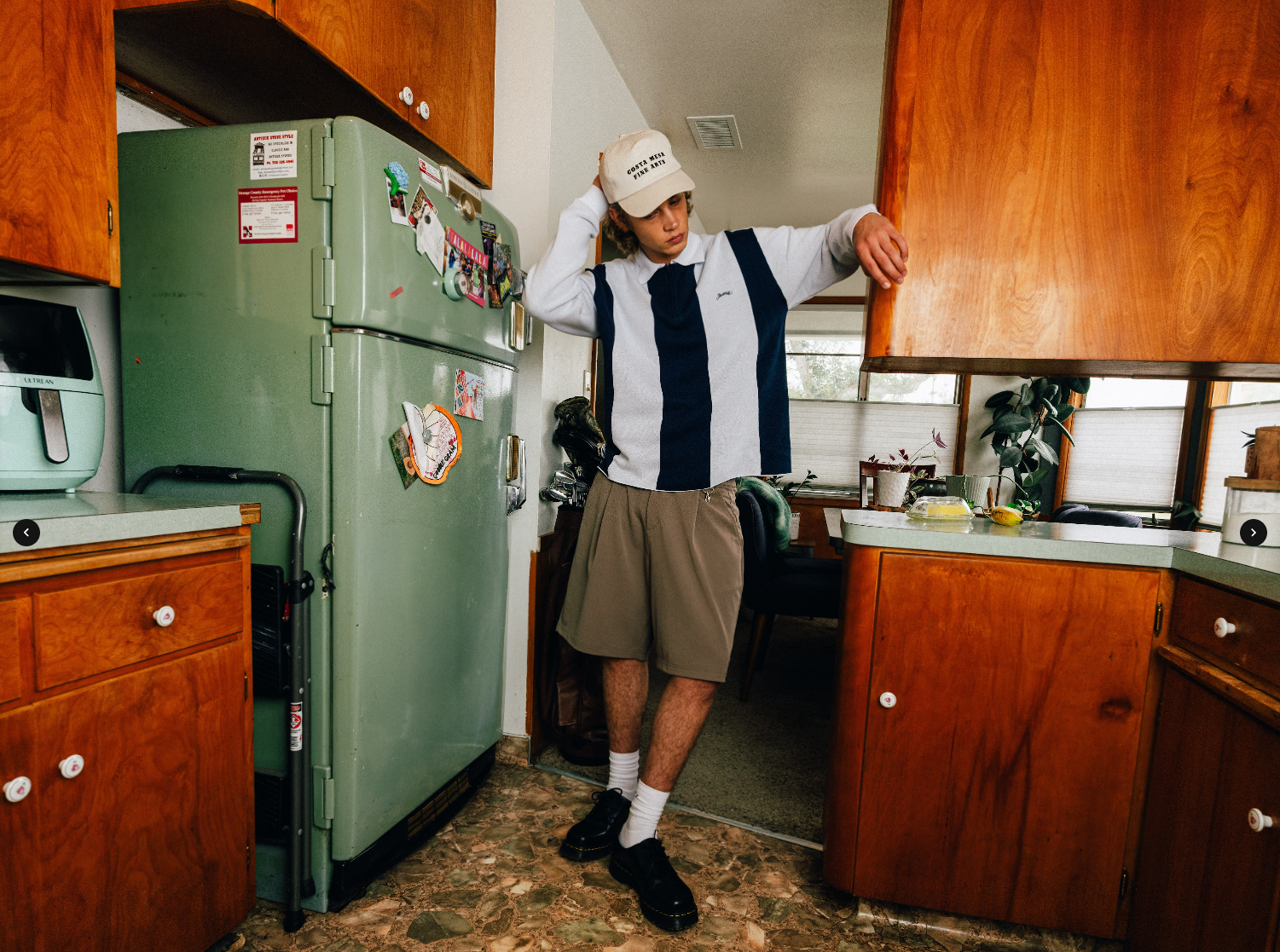 Person in a kitchen with wooden cabinets and a green refrigerator.