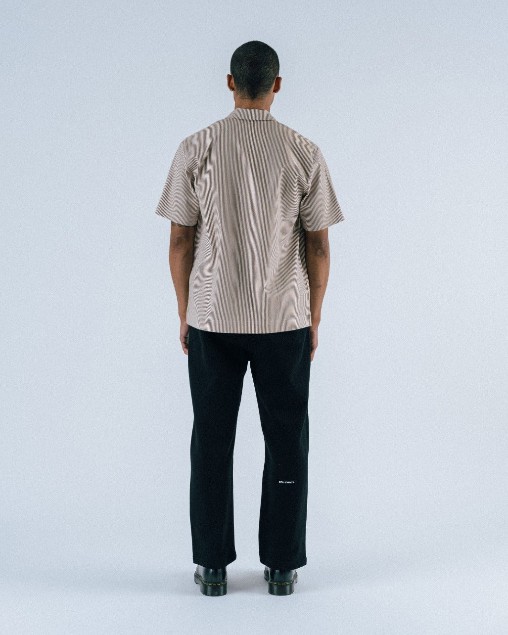 Person wearing a beige short-sleeve shirt and black pants on a white background