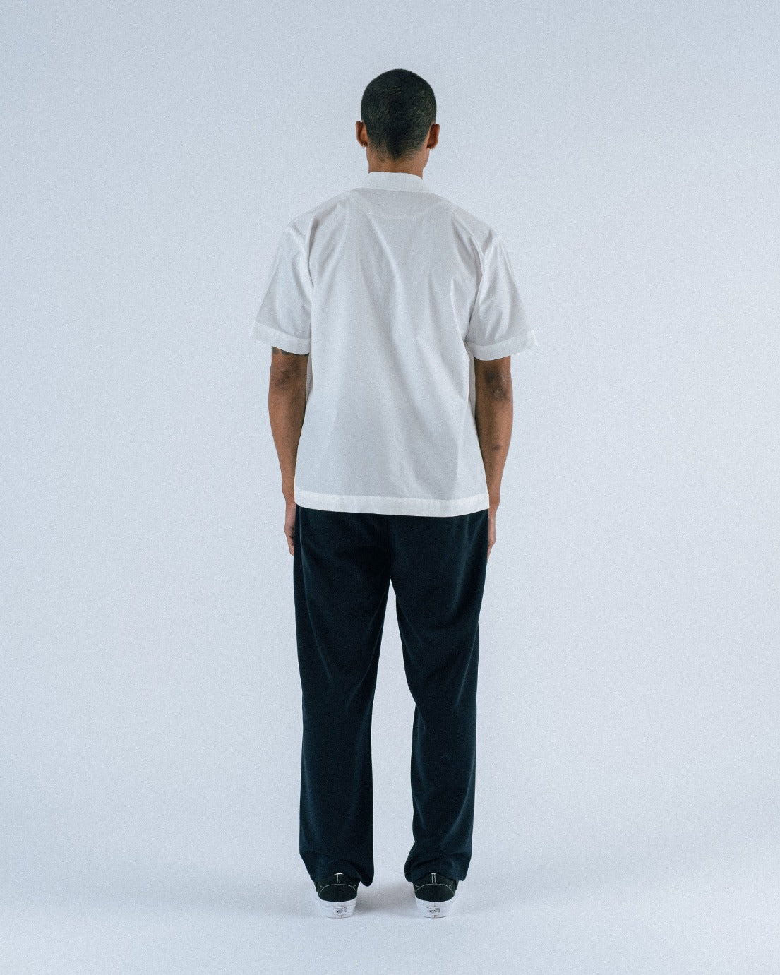 Person wearing a white t-shirt and dark pants on a light gray background