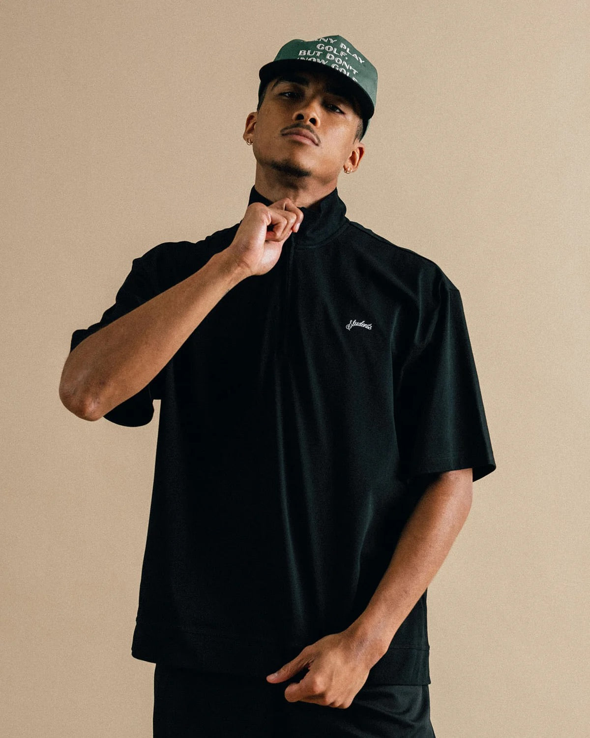 Man wearing a black outfit with a brand logo on a beige background