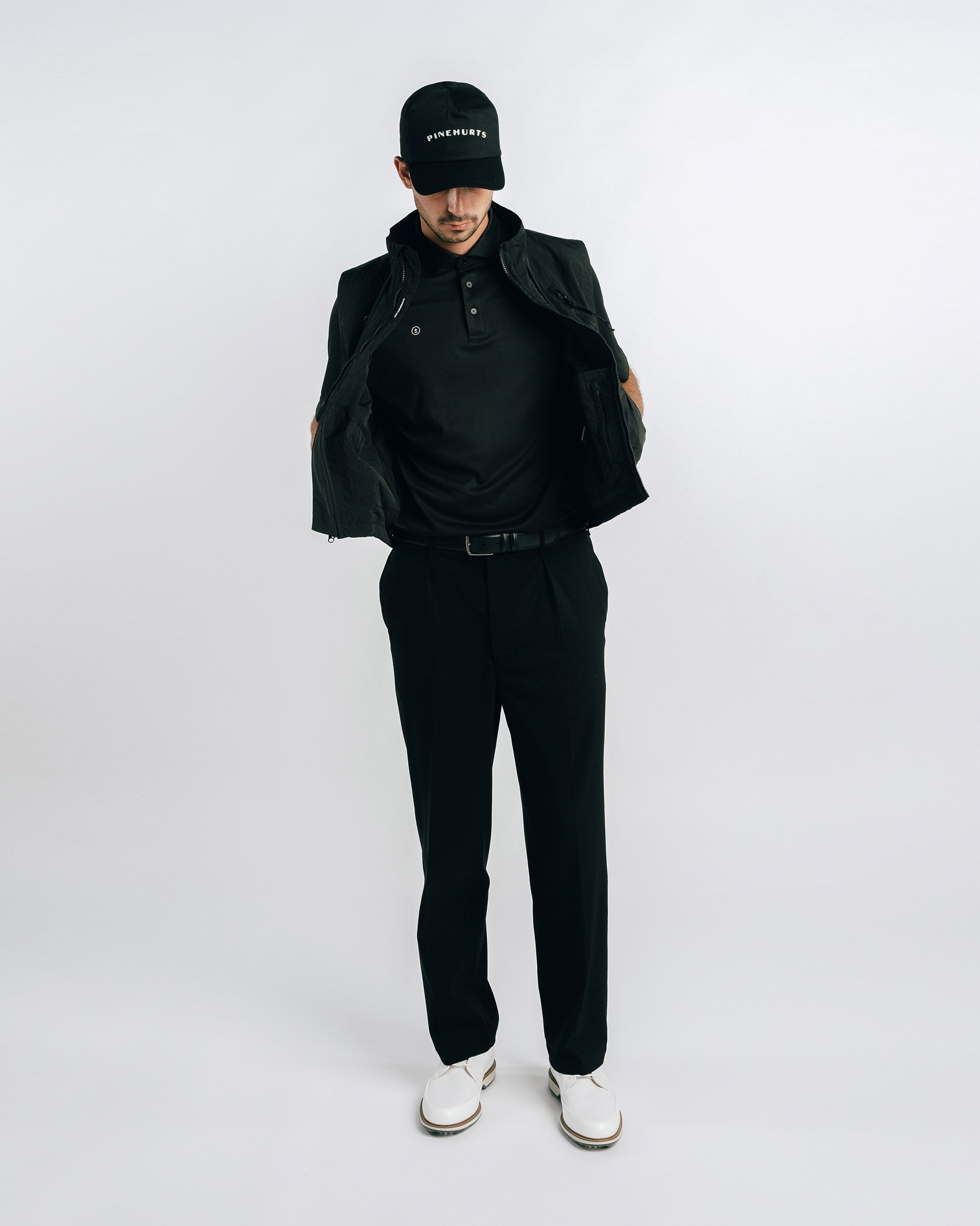 Person wearing a black outfit with a jacket, shirt, pants, and cap on a white background