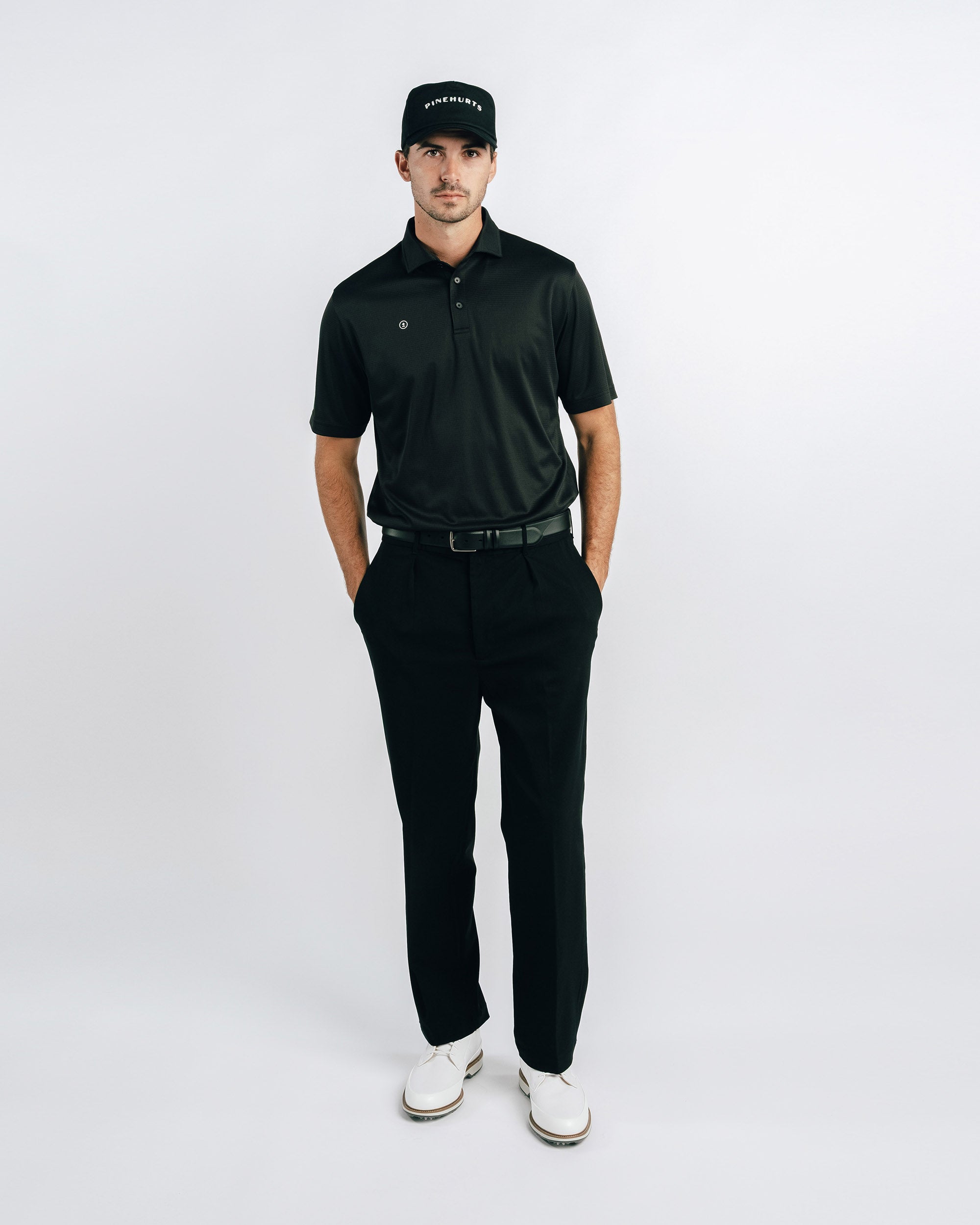 Man wearing a black polo shirt, black pants, and white shoes on a white background