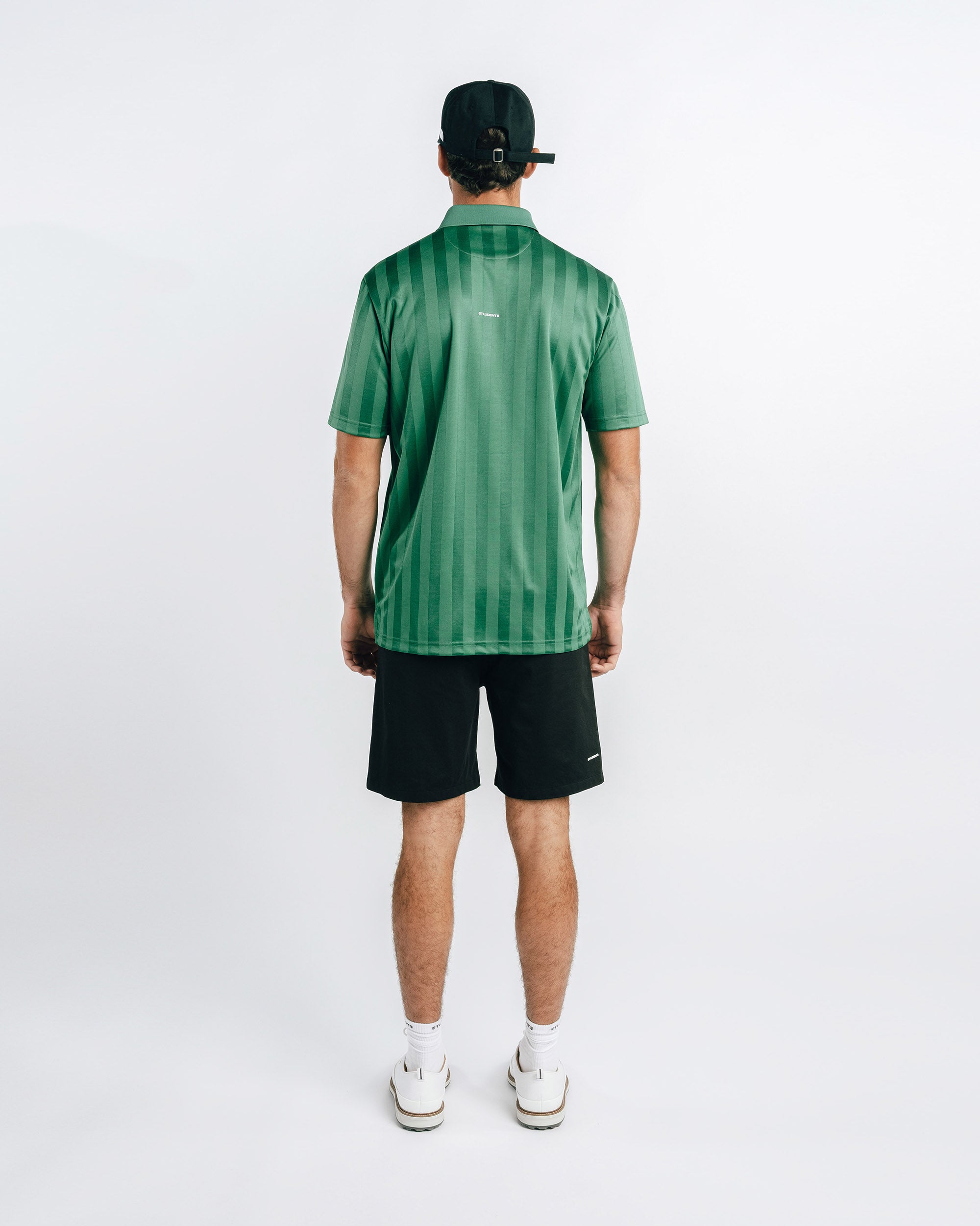 Person wearing a green striped polo shirt and black shorts on a white background