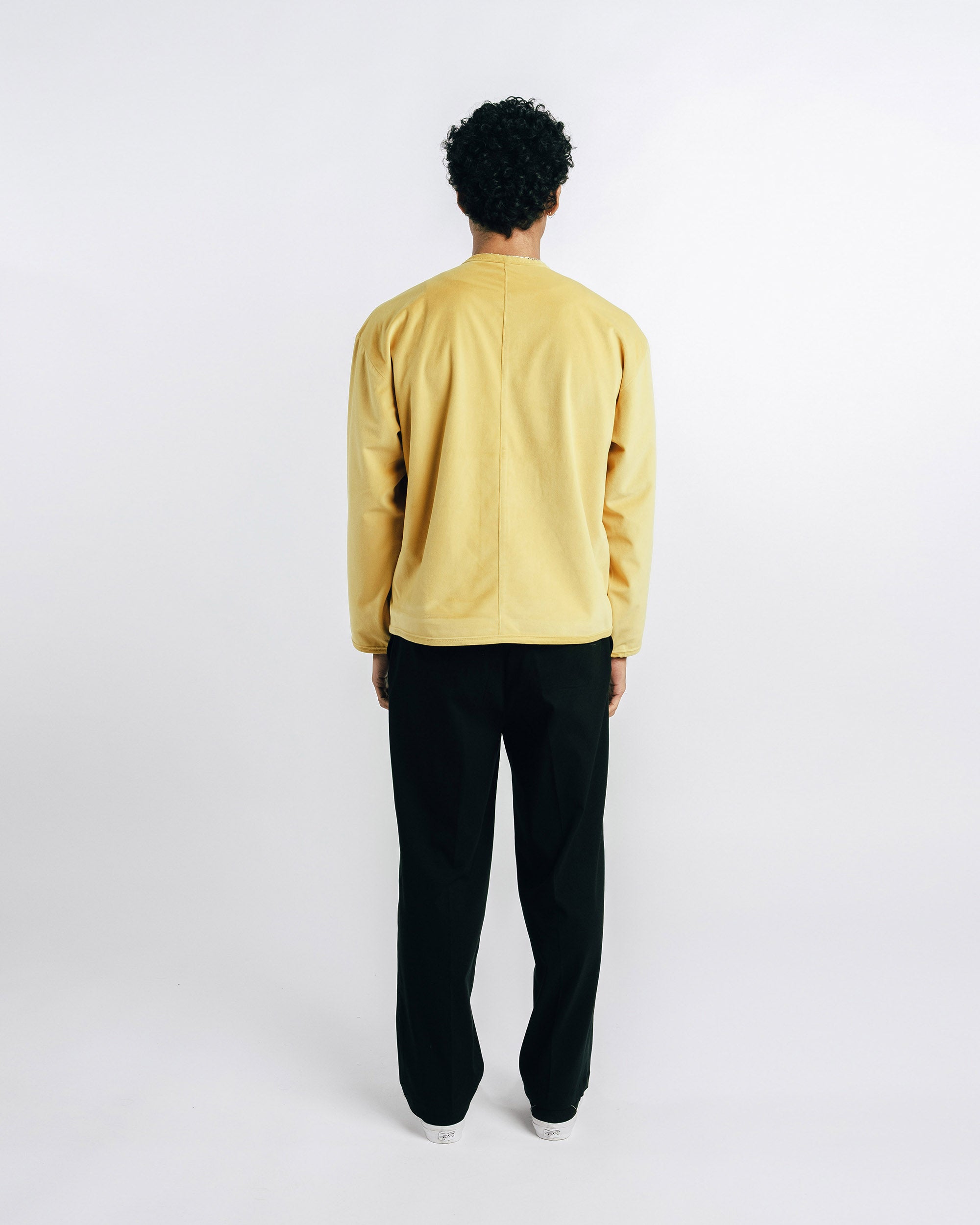 Person wearing a mustard yellow jacket, white shirt, black pants, and black shoes on a white background