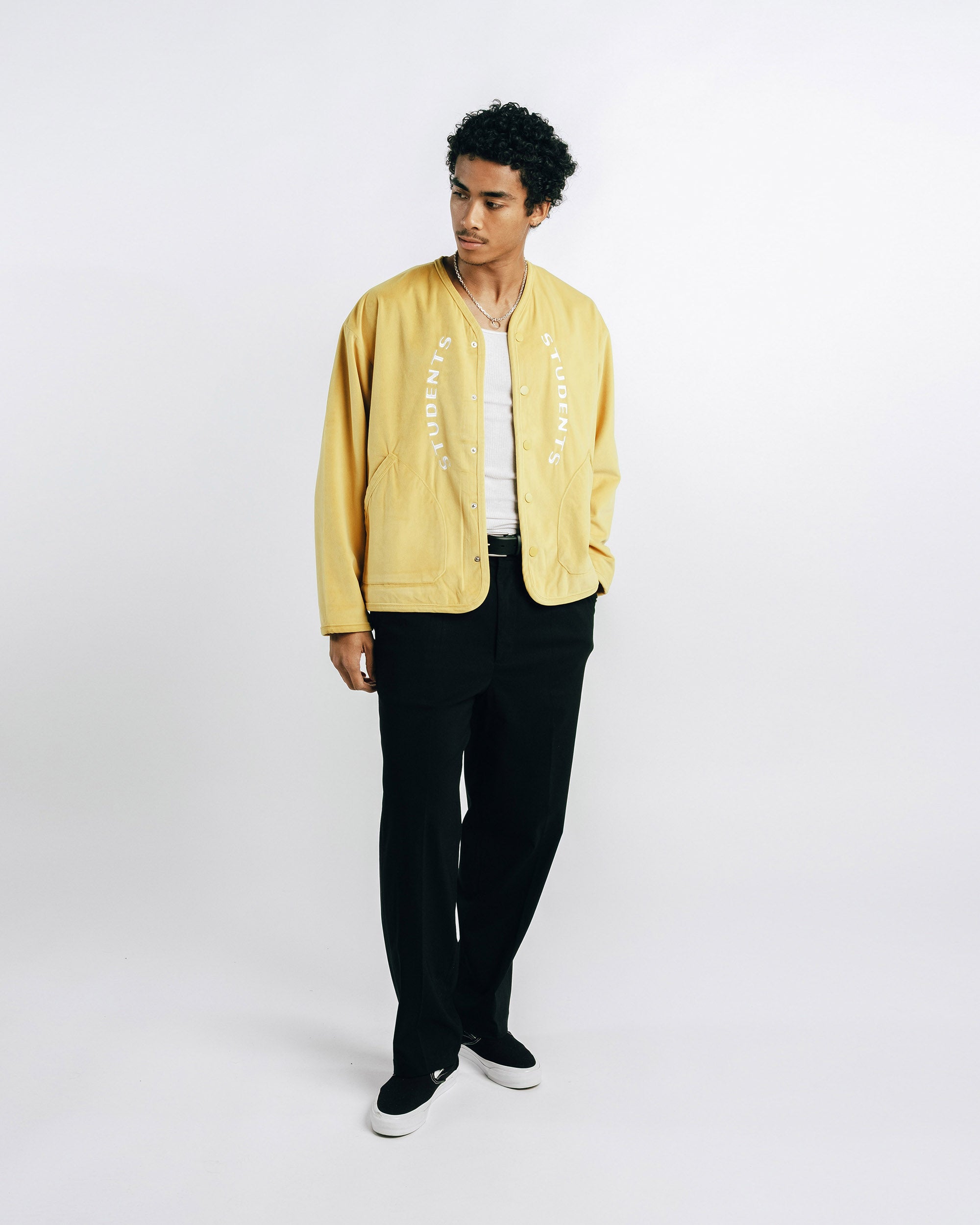 Person wearing a mustard yellow jacket, white shirt, black pants, and black shoes on a white background