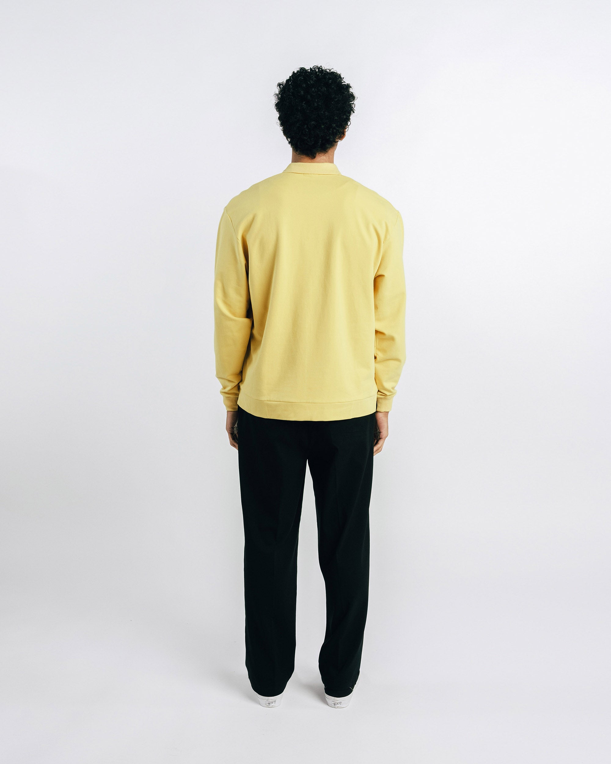 Person wearing a yellow sweater and black pants on a white background
