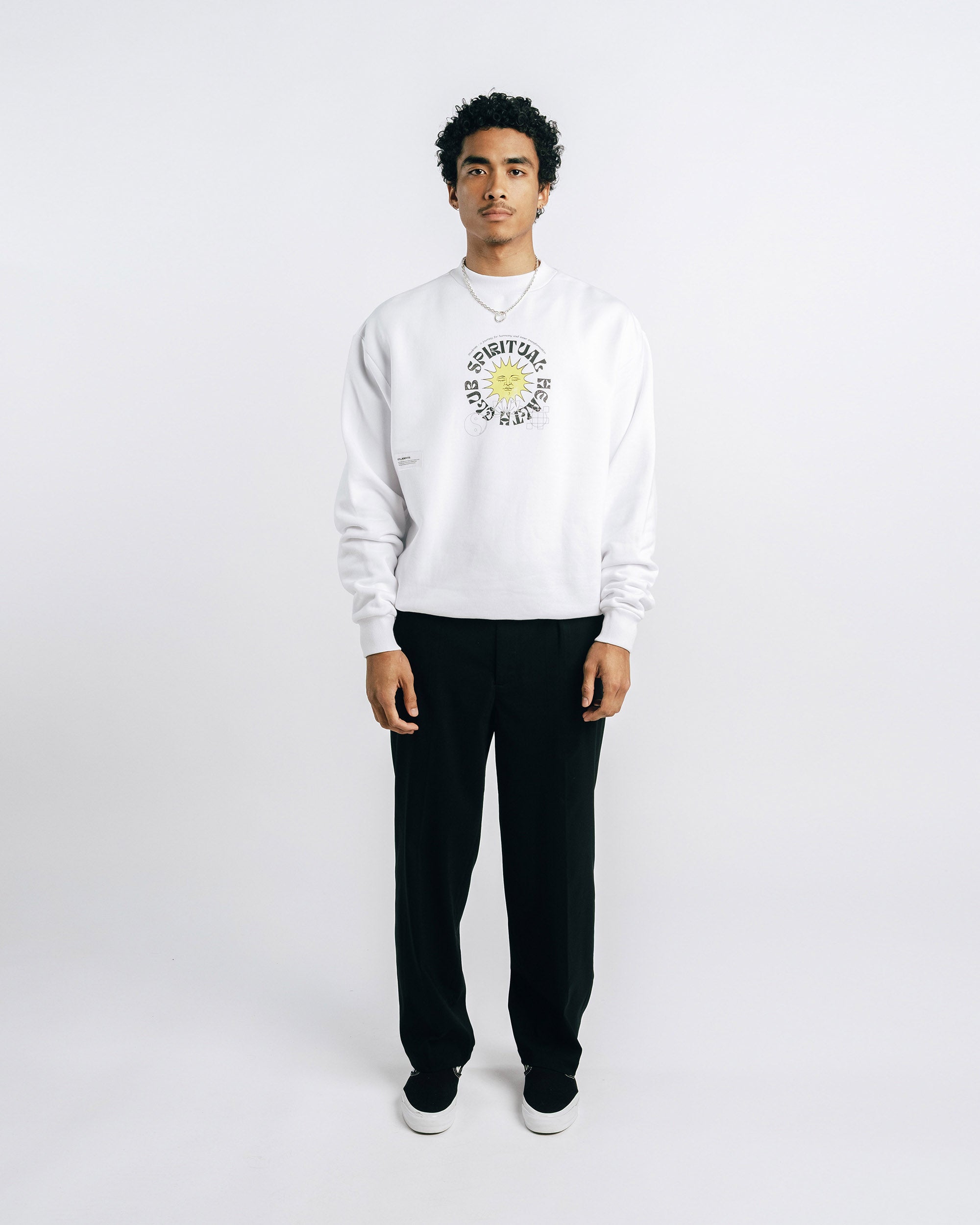 Person wearing a white sweatshirt with a logo and black pants on a white background
