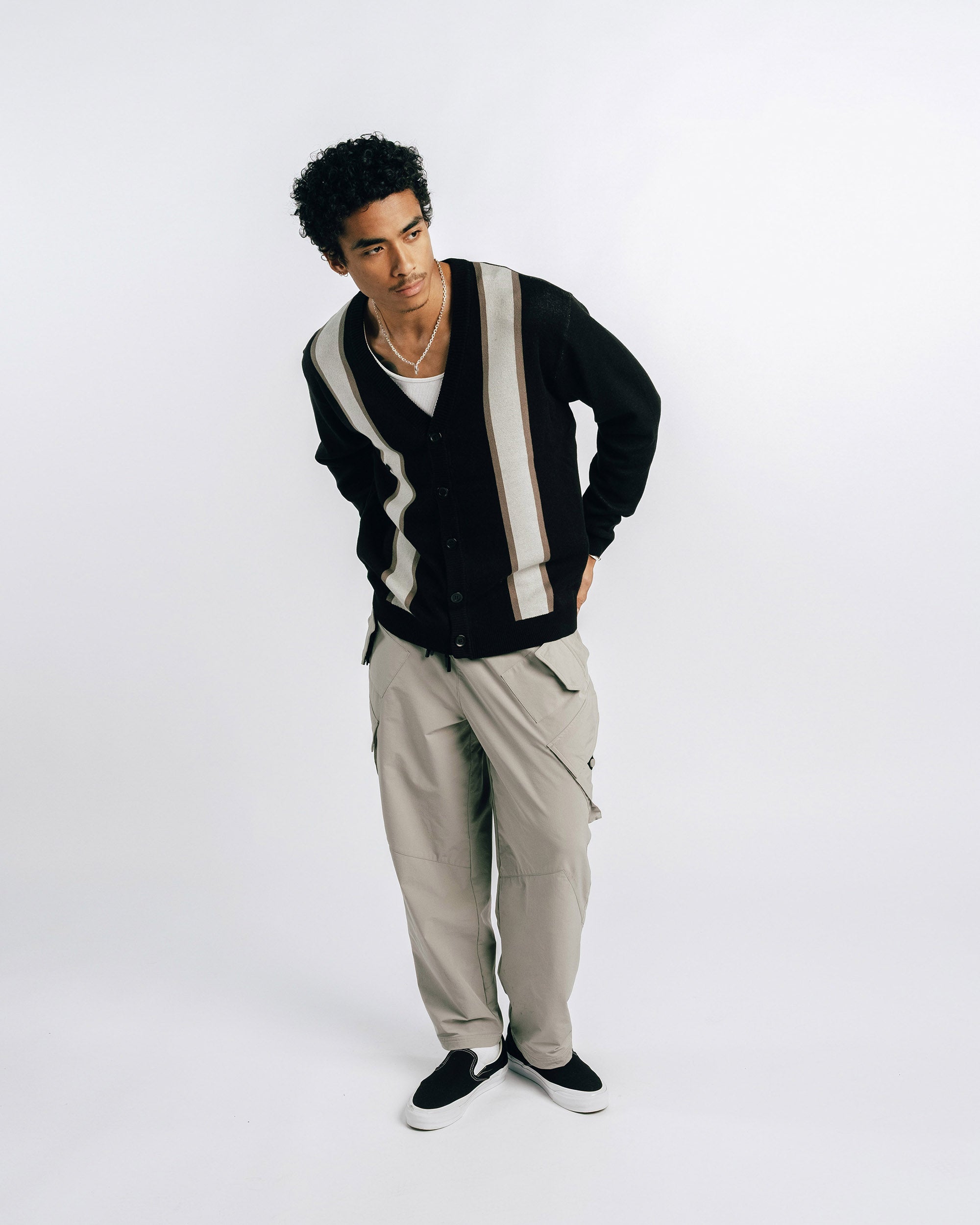 Person wearing a black and white striped cardigan with beige pants on a white background