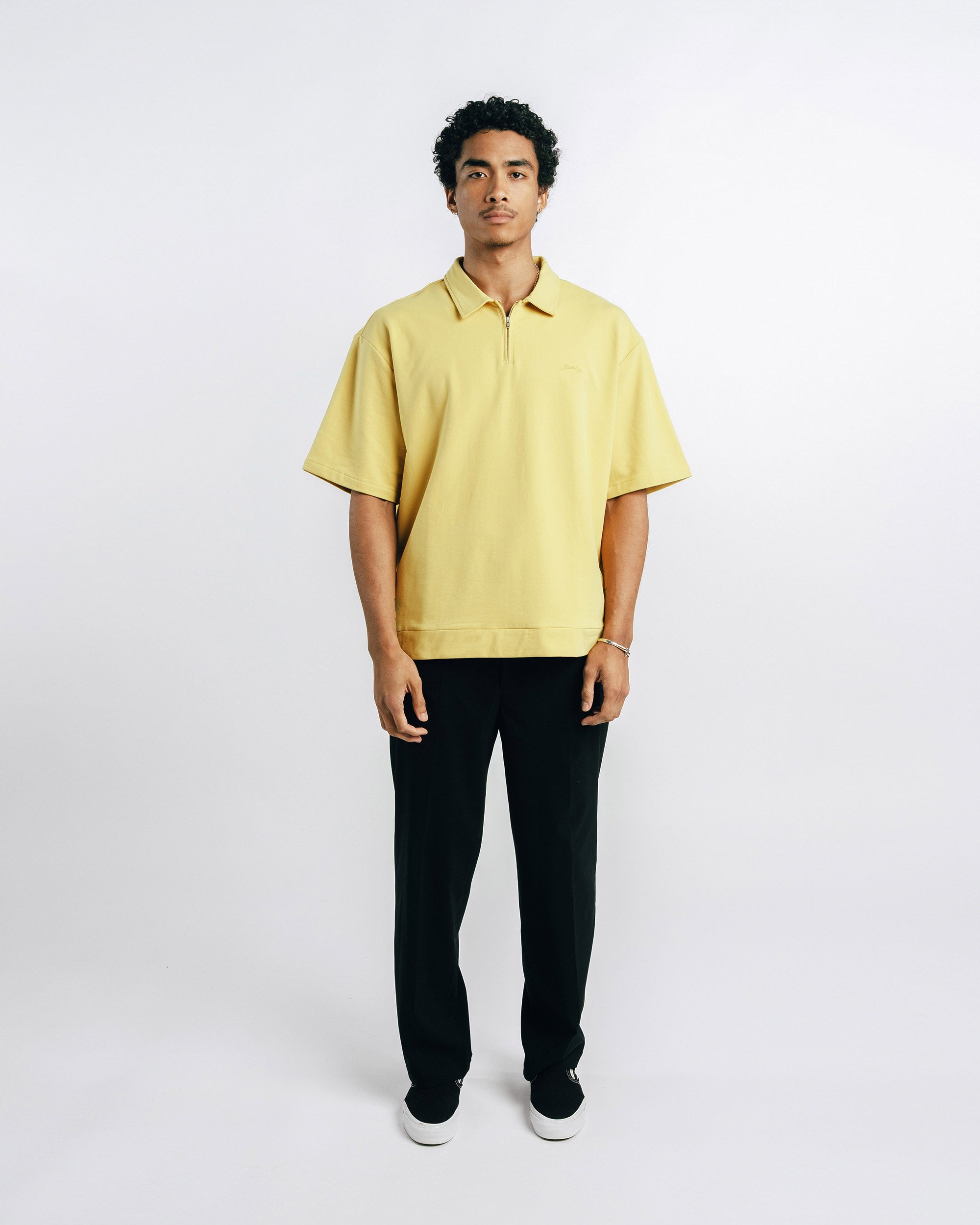 Man wearing a yellow polo shirt and black pants on a white background