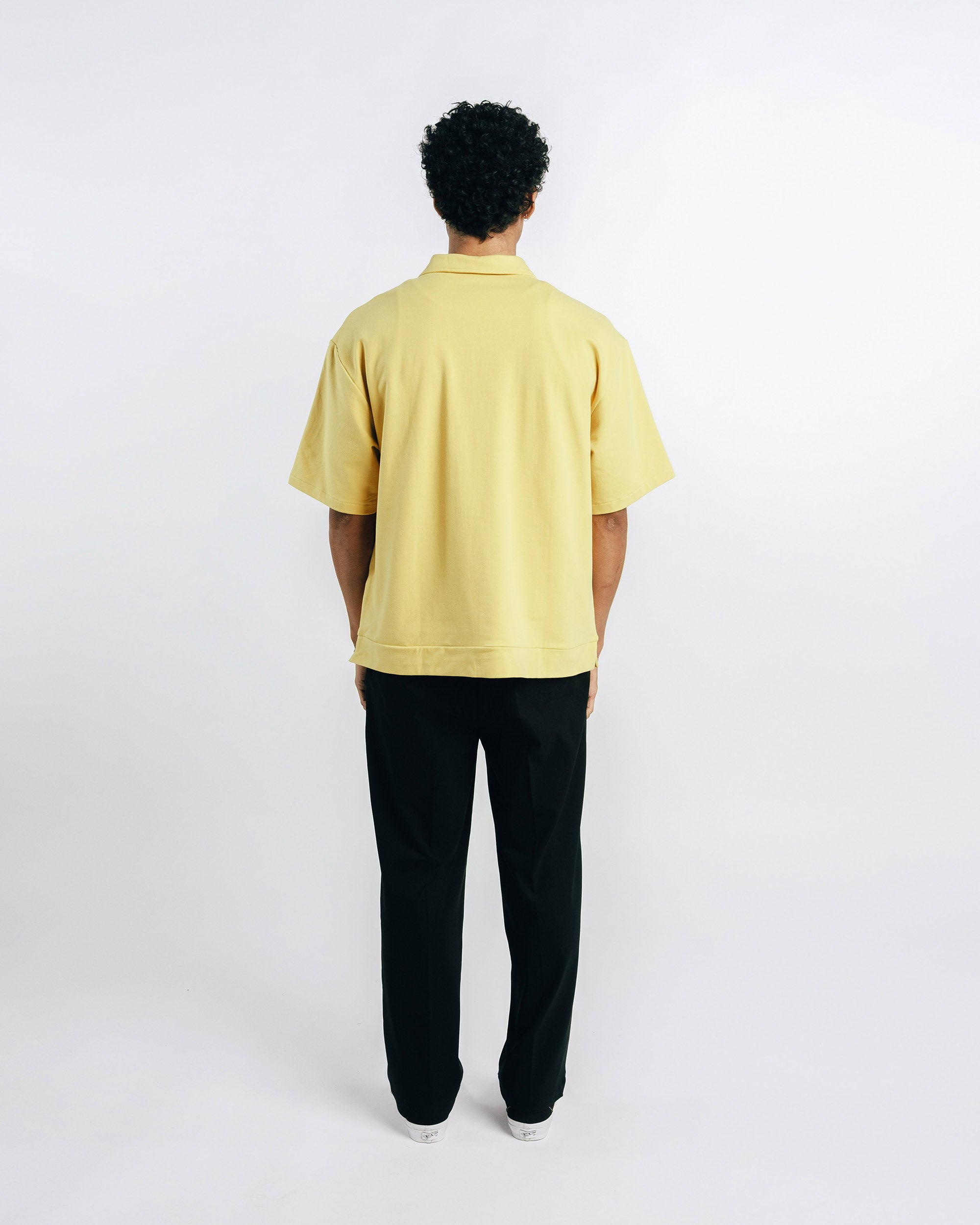 Person wearing a yellow shirt and black pants on a white background