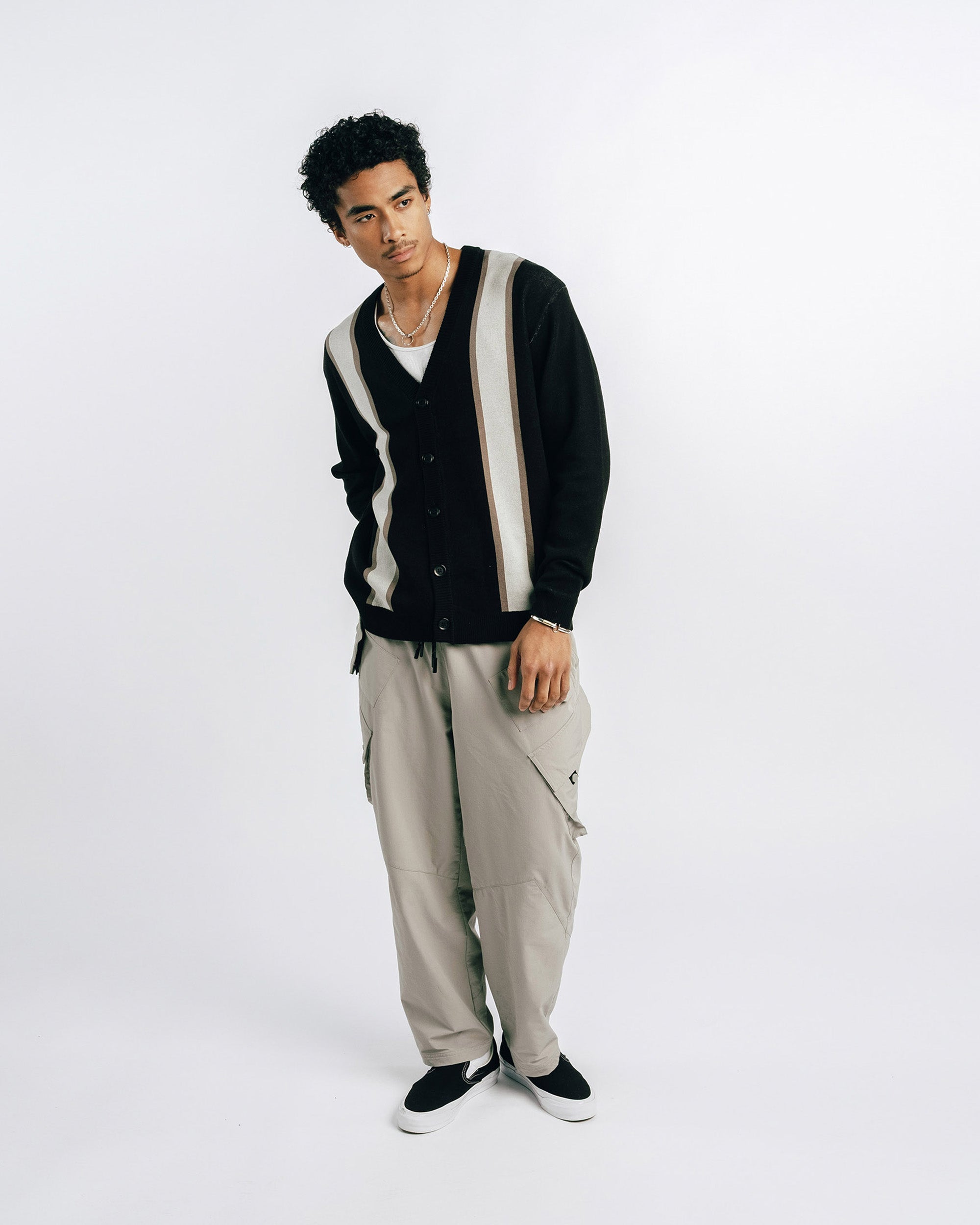 Person wearing a black and white striped cardigan with beige pants on a white background