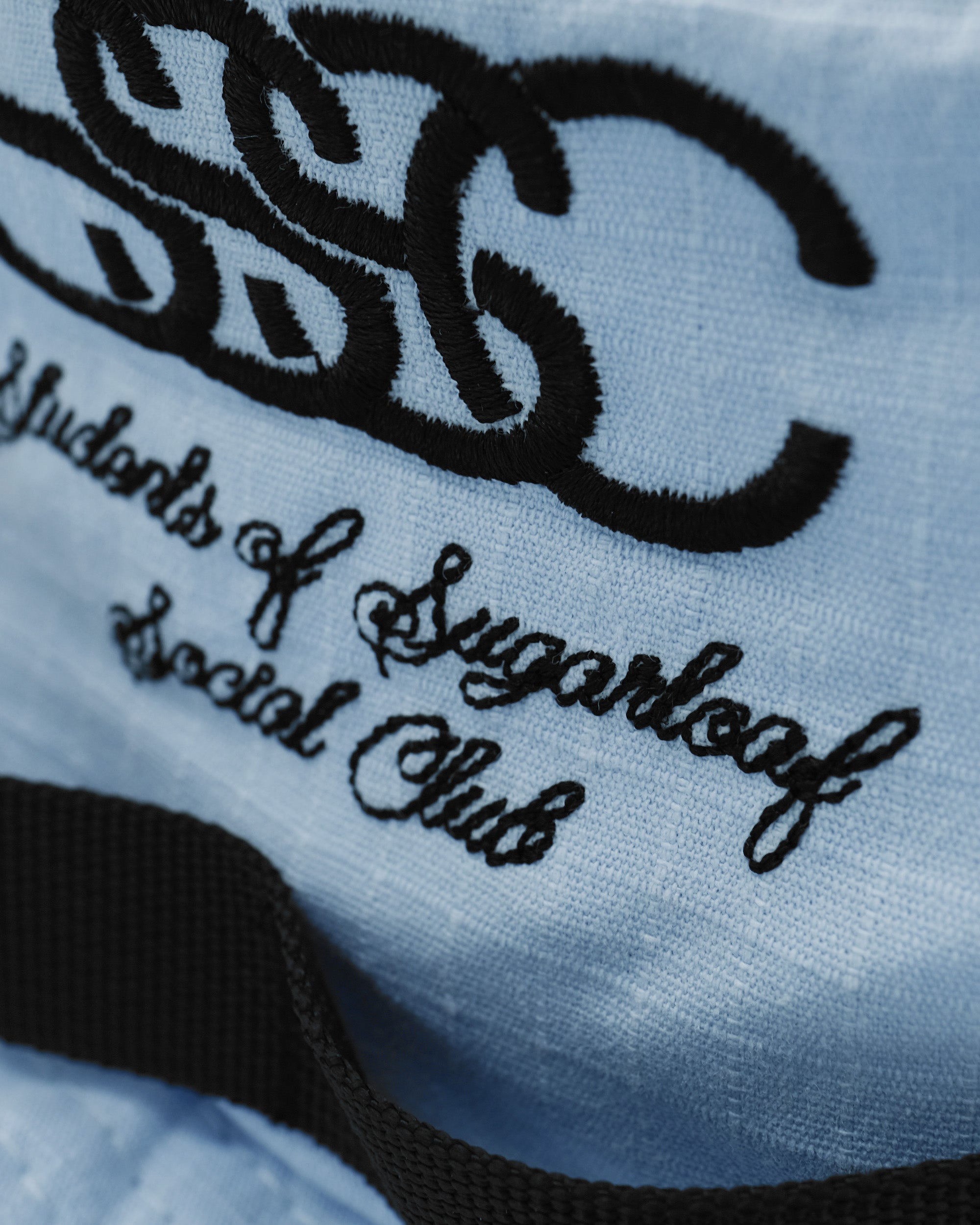 Close-up of a blue fabric with black text and logo, featuring 'Students of Sugarloaf Social Club'.