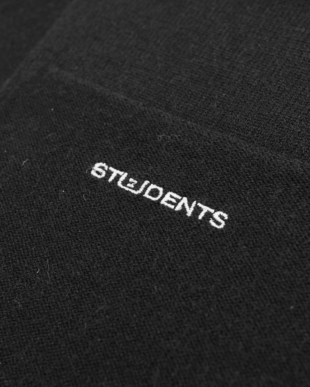 Close-up of a black knit fabric with the word 'STUDENTS' embroidered in white across the center.