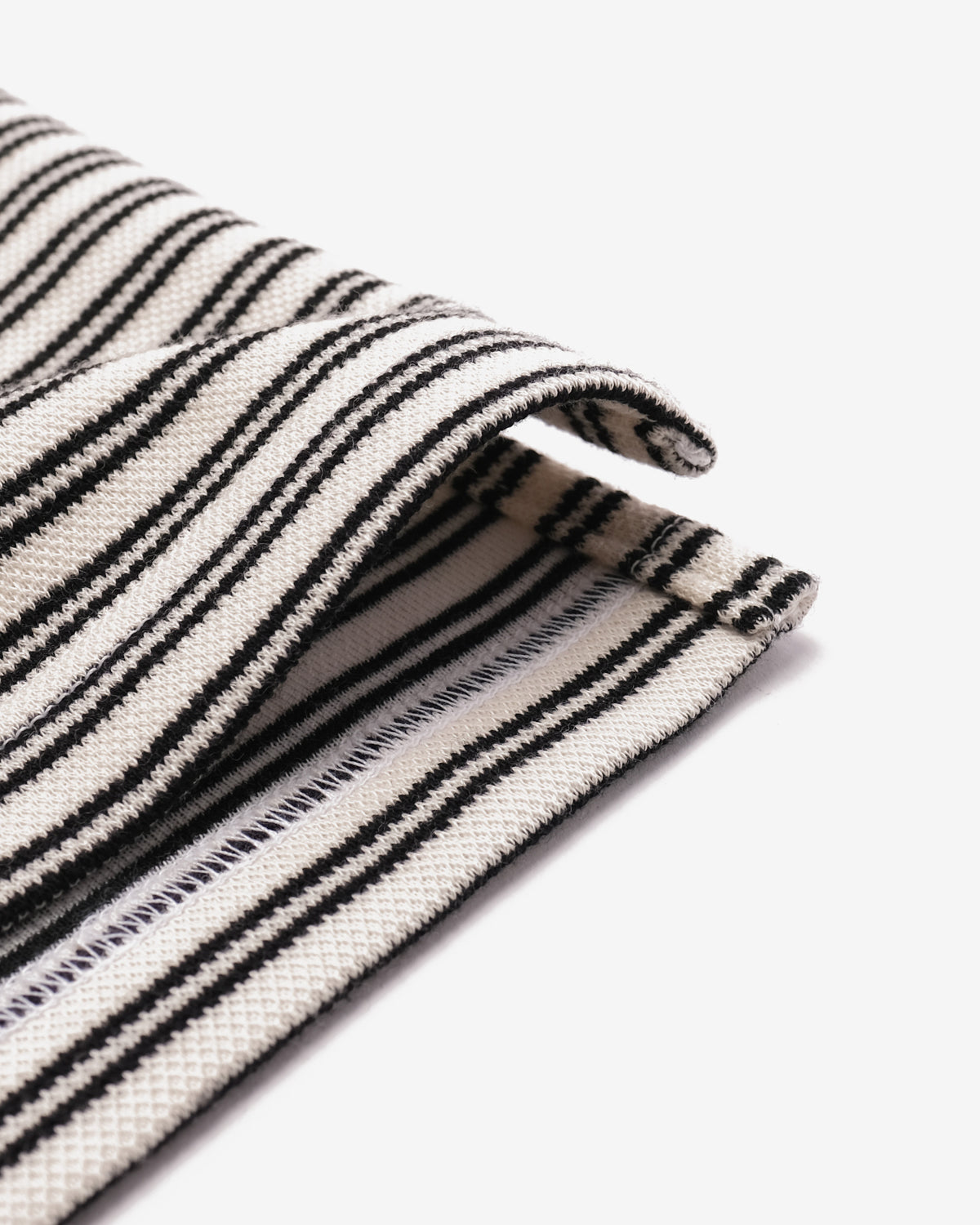A close-up of a folded woven textile with narrow black stripes on an off-white base, shown against a clean white background.