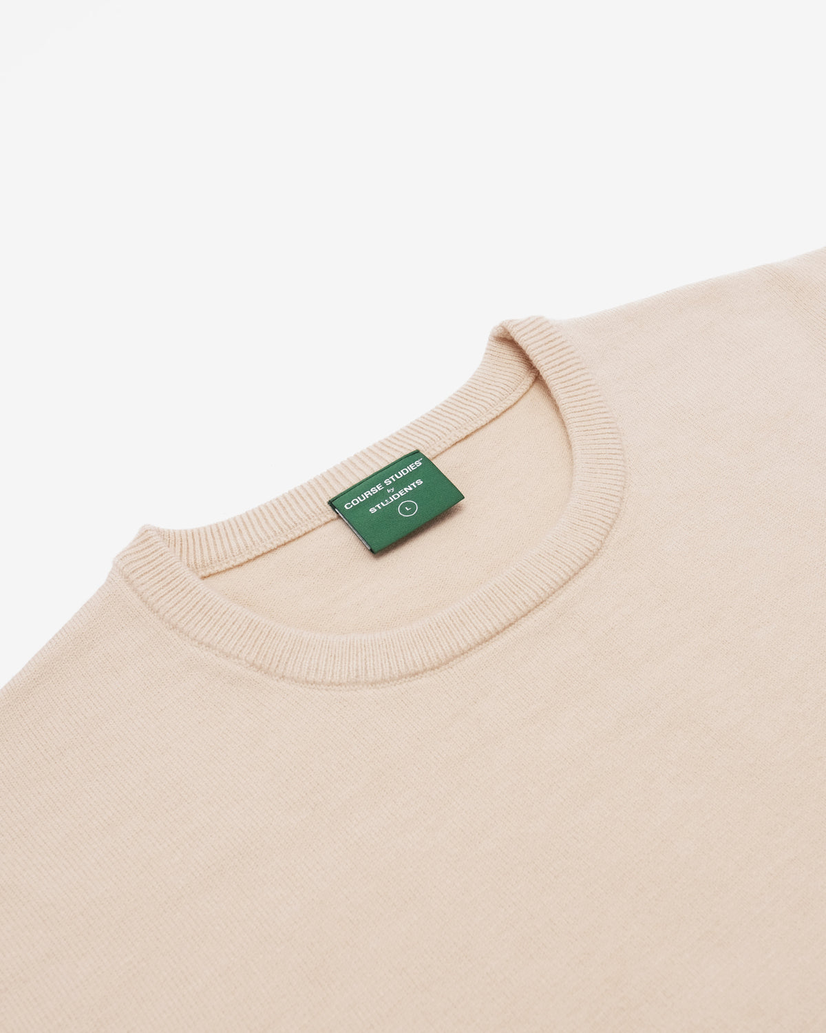 Close-up of a cream-colored crewneck sweater with a green brand tag reading 'Fossil / Fossil Denmark' inside the ribbed collar.
