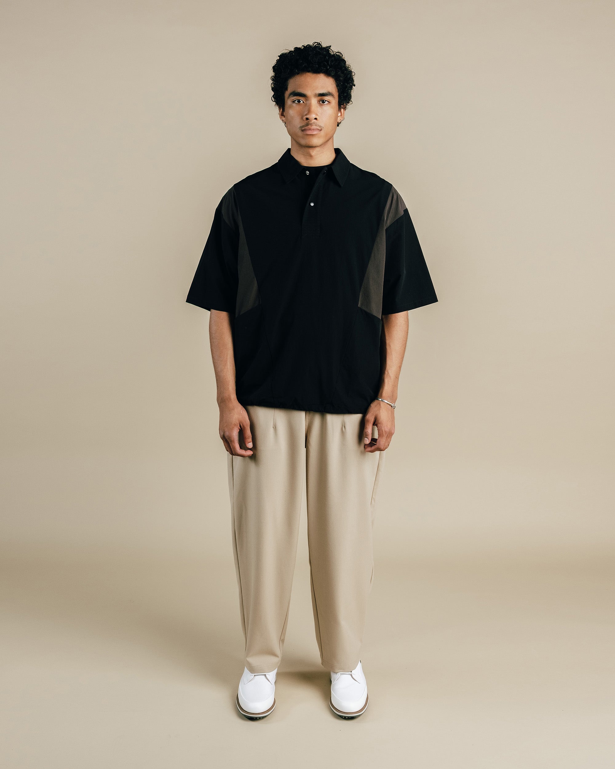 Man wearing a black and gray shirt with beige pants on a beige background