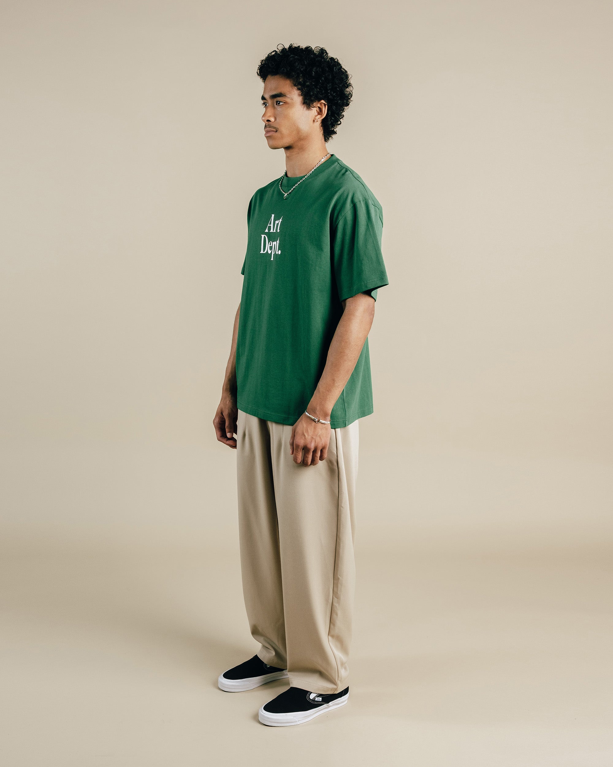 Person wearing a green t-shirt with text and beige pants on a beige background