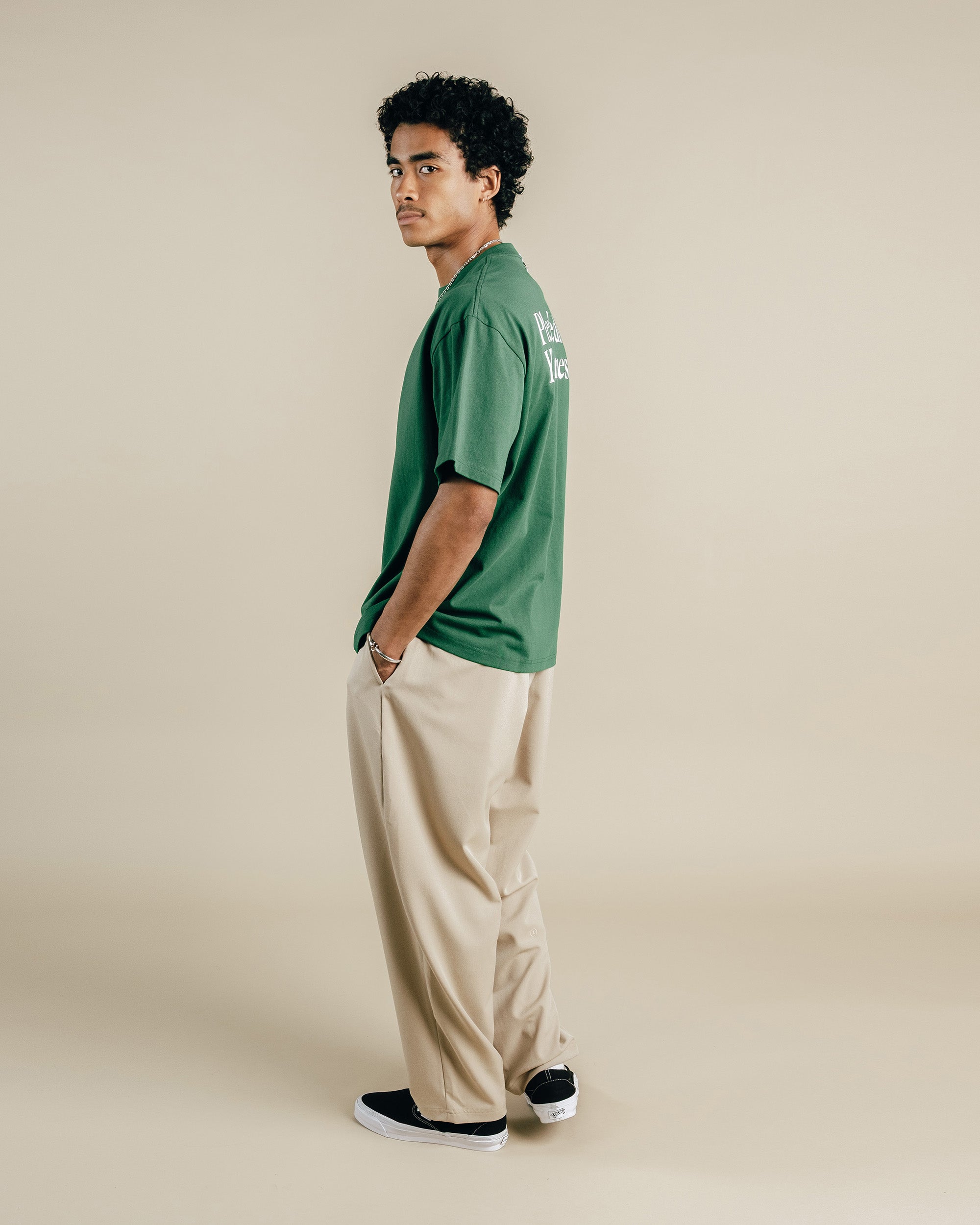 Man wearing a green shirt and beige pants against a beige background