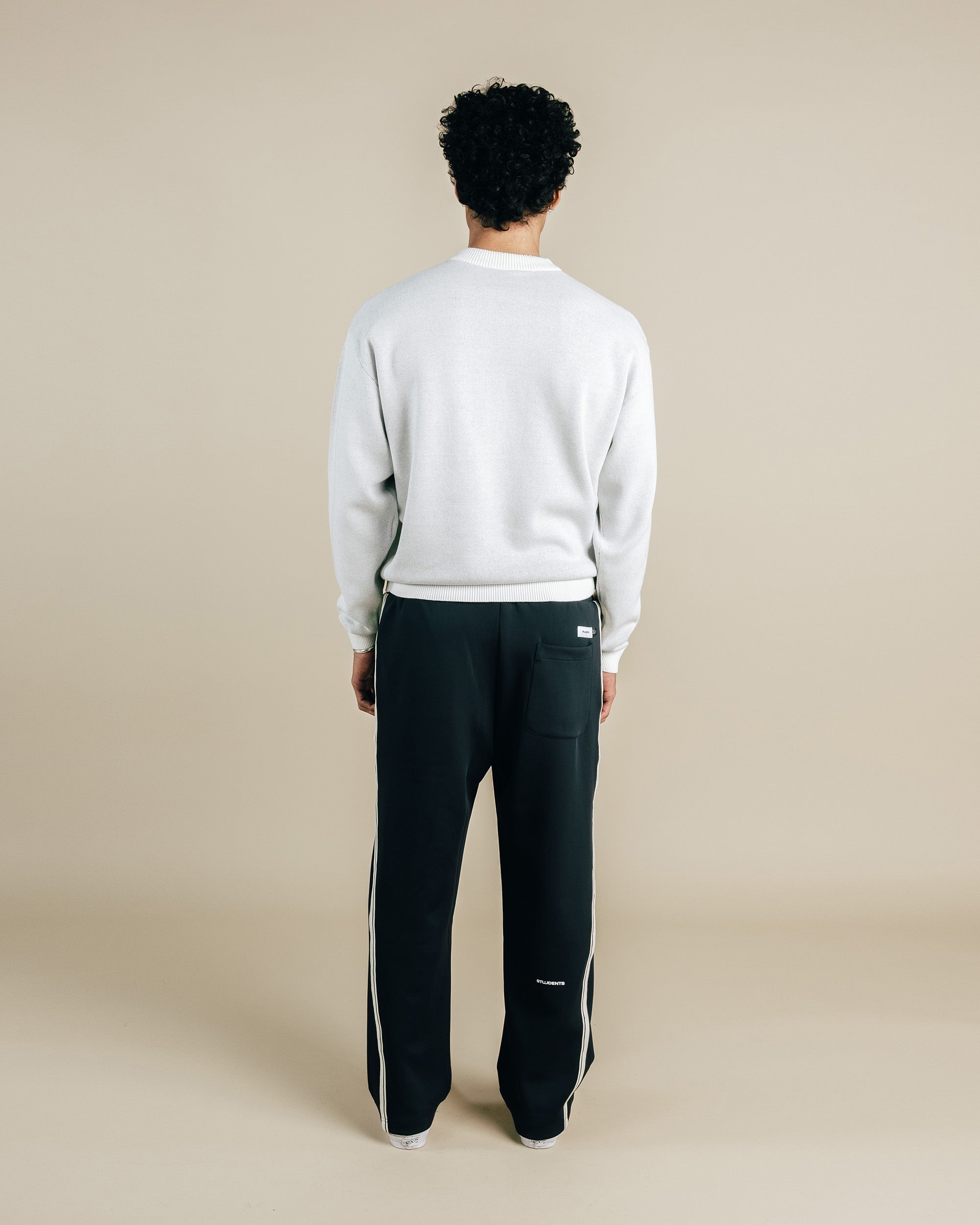 Person wearing a light gray sweatshirt and black pants with white stripes on a beige background