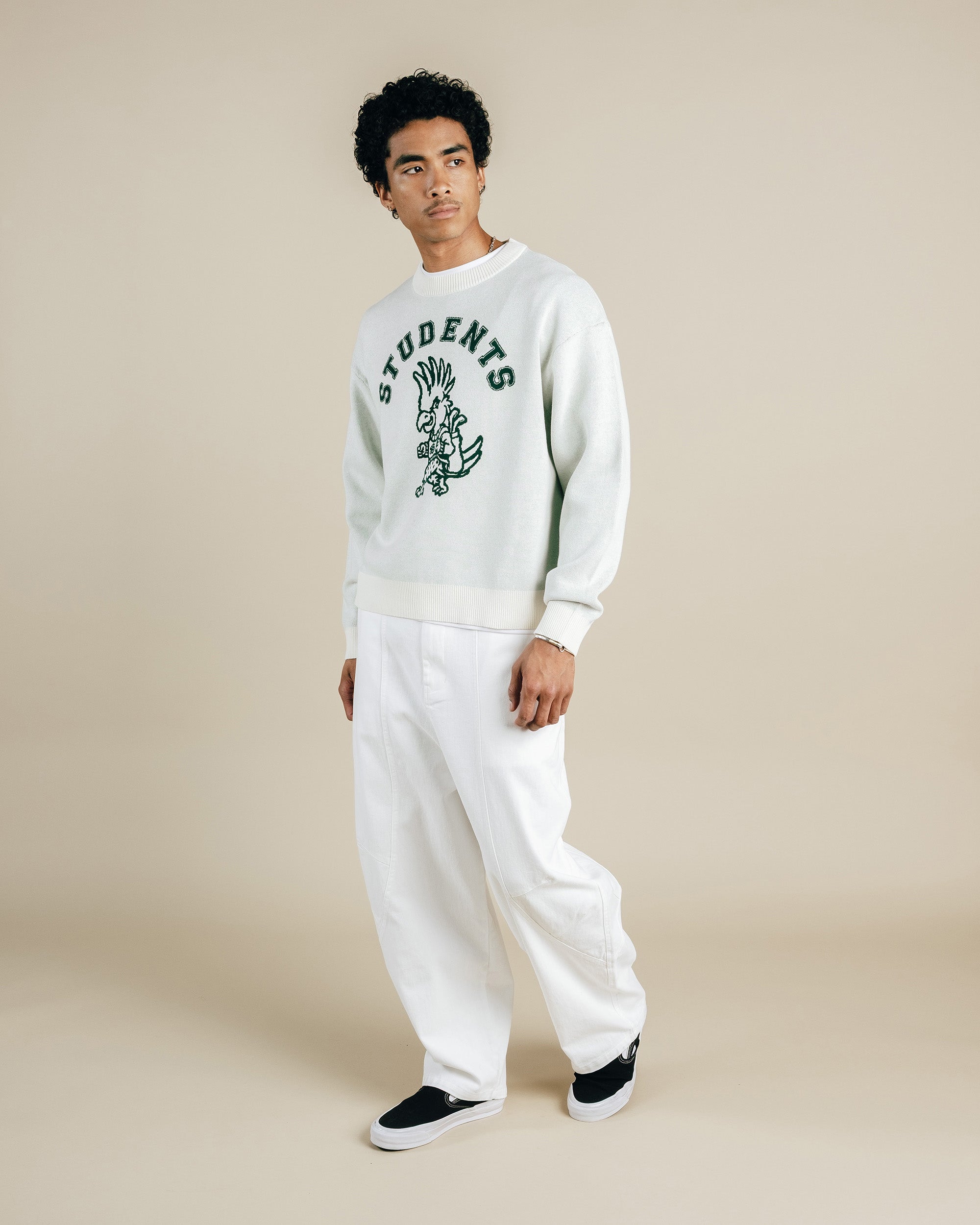 Person wearing a white sweater with text and graphics, paired with white pants on a beige background