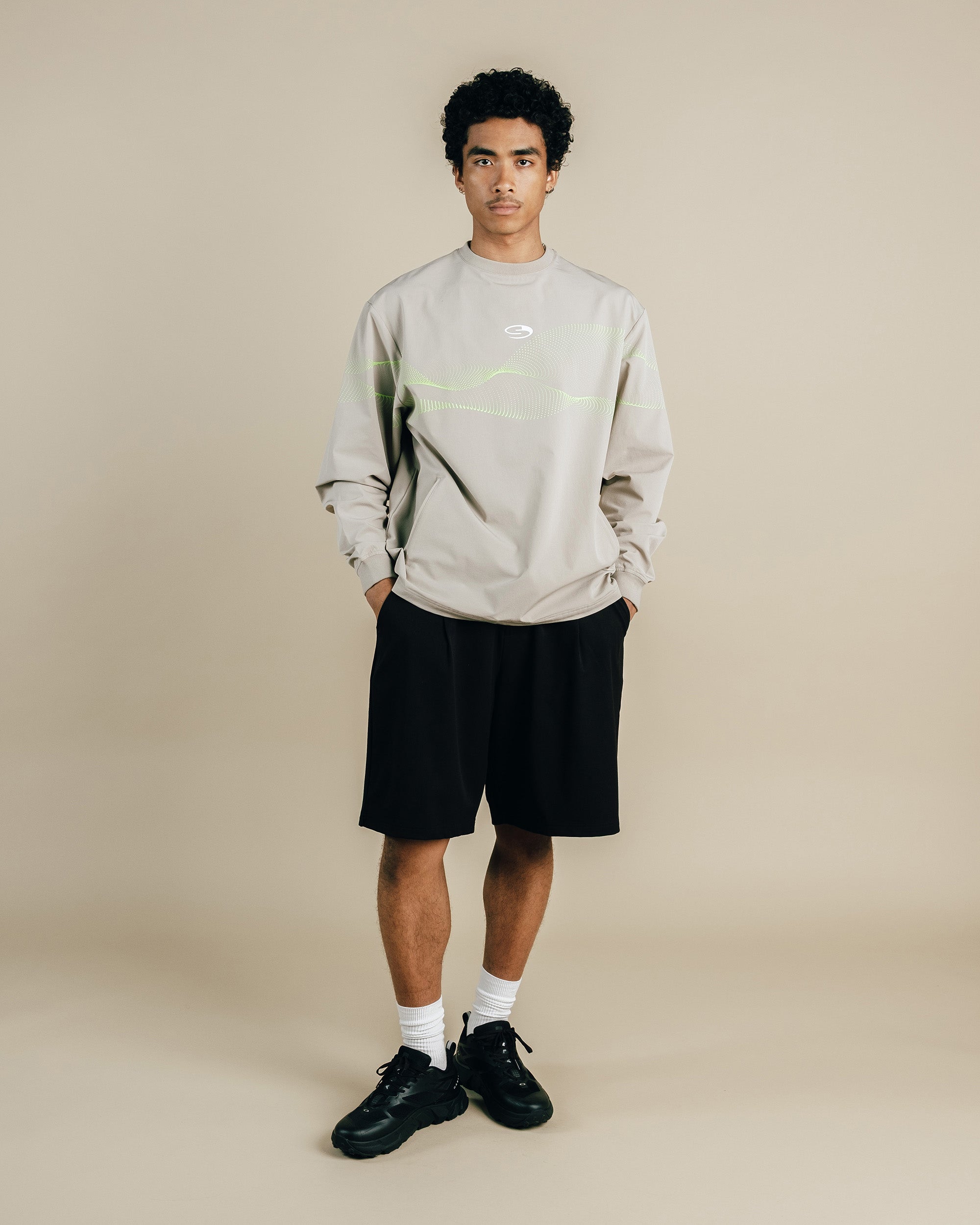 Person wearing a light gray sweatshirt with a logo and black shorts on a beige background