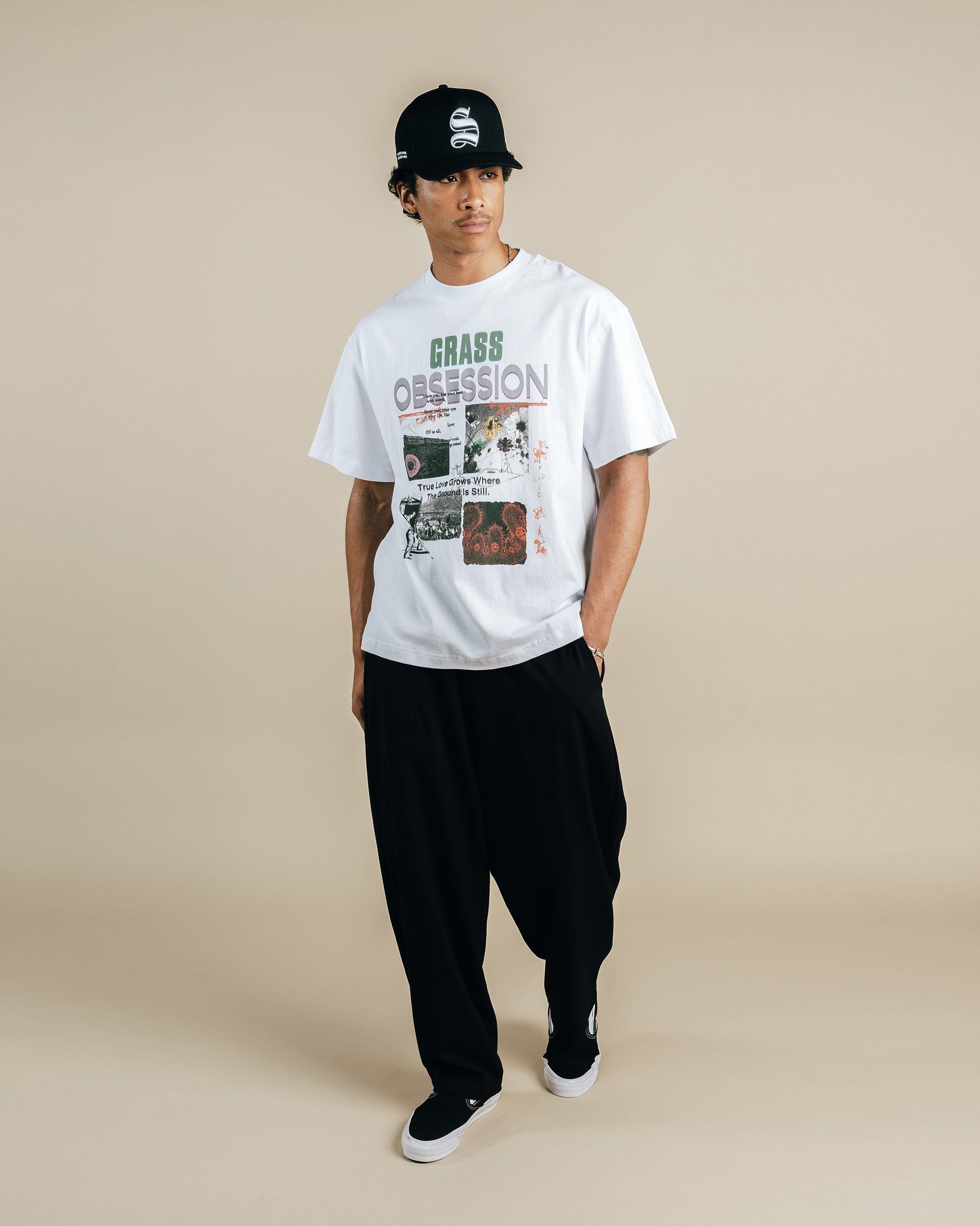 Person wearing a white graphic t-shirt and black pants on a beige background