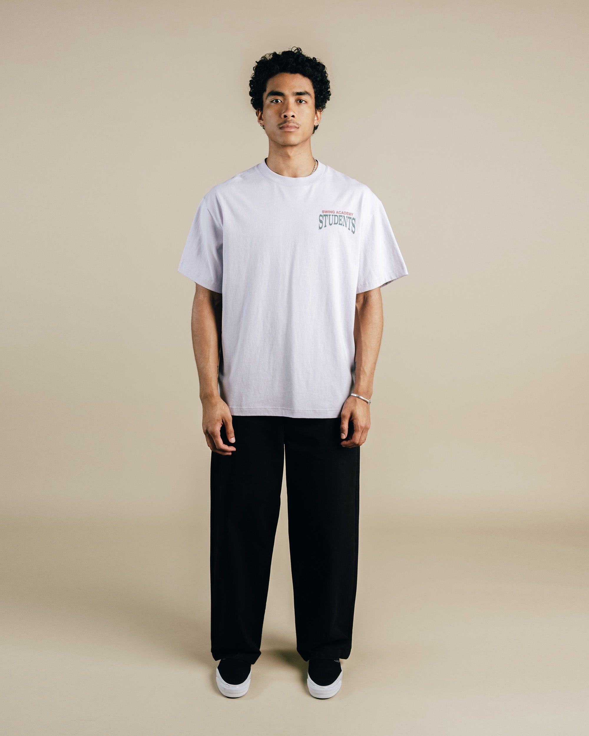 Person wearing a light purple t-shirt with text and black pants on a beige background