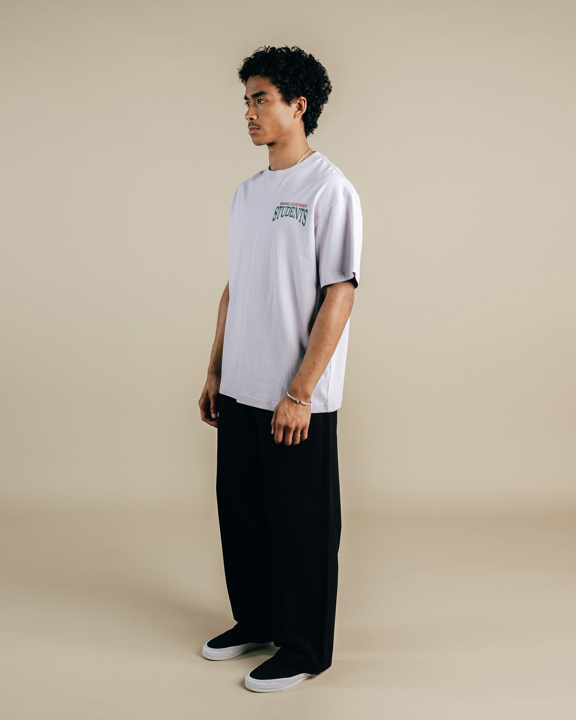 Person wearing a light purple t-shirt with text and black pants on a beige background