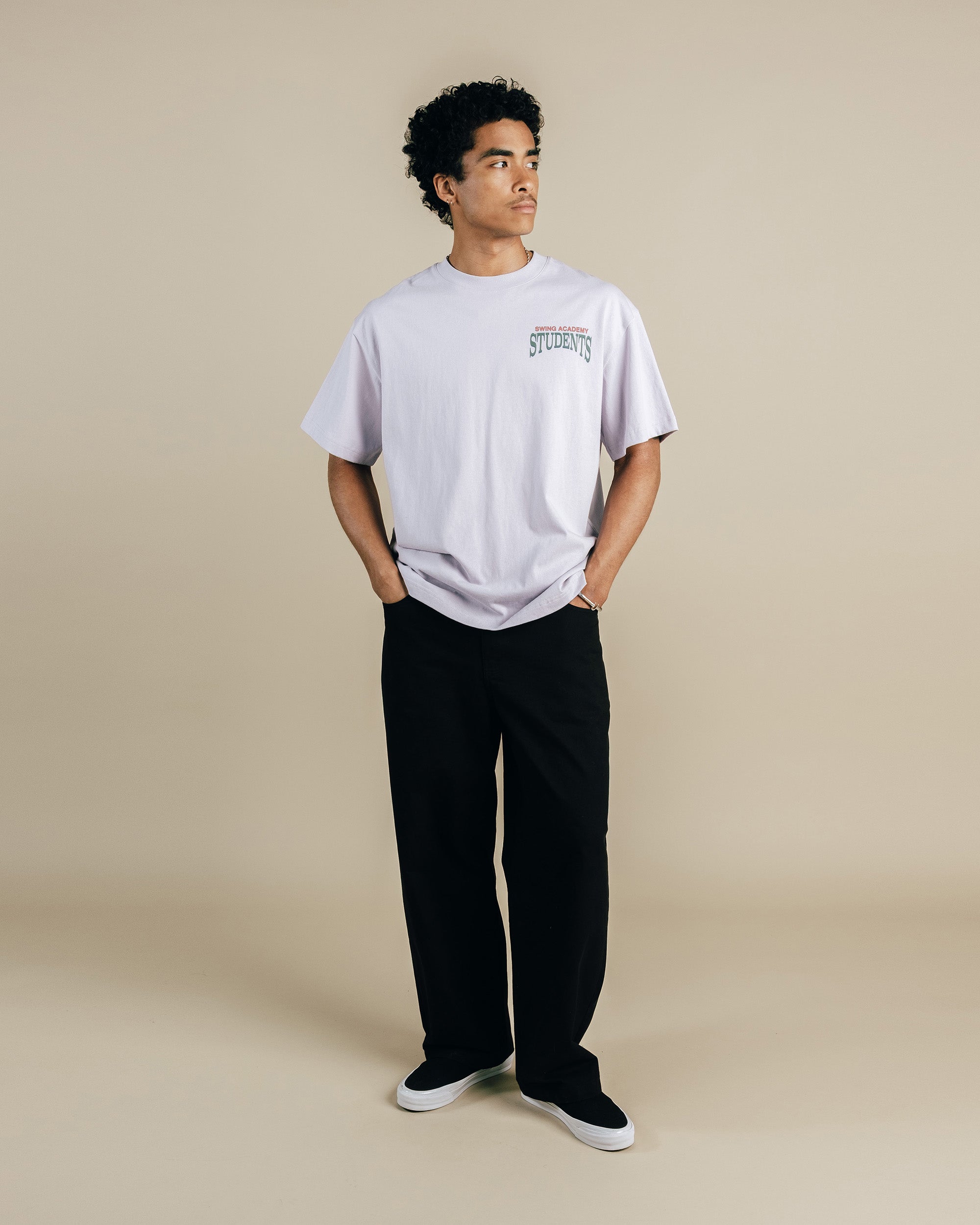 Person wearing a light purple t-shirt and black pants on a beige background