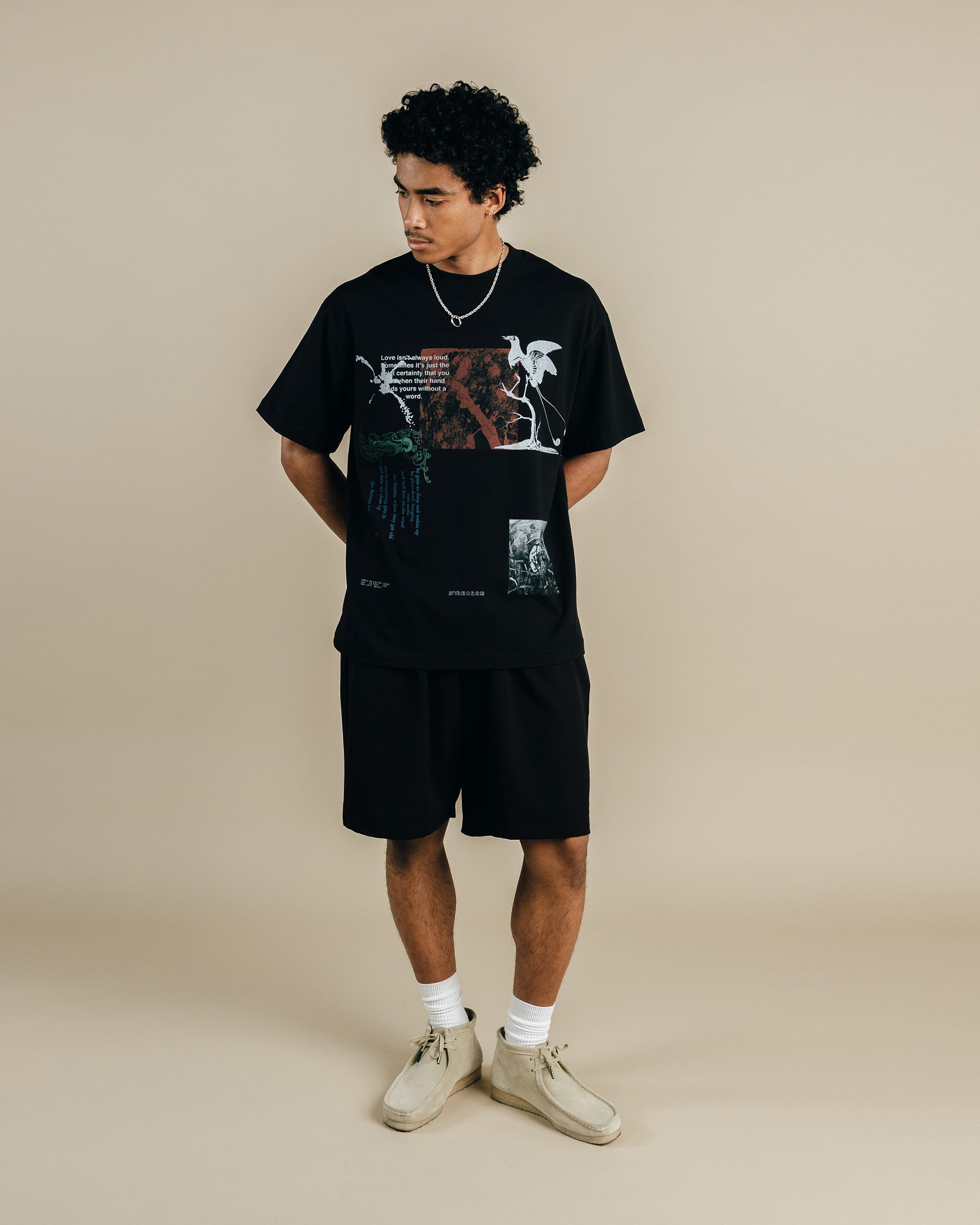 Person wearing a black graphic t-shirt and shorts on a beige background