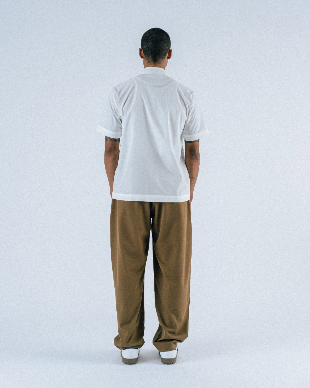 Person wearing a white shirt and brown pants on a light gray background