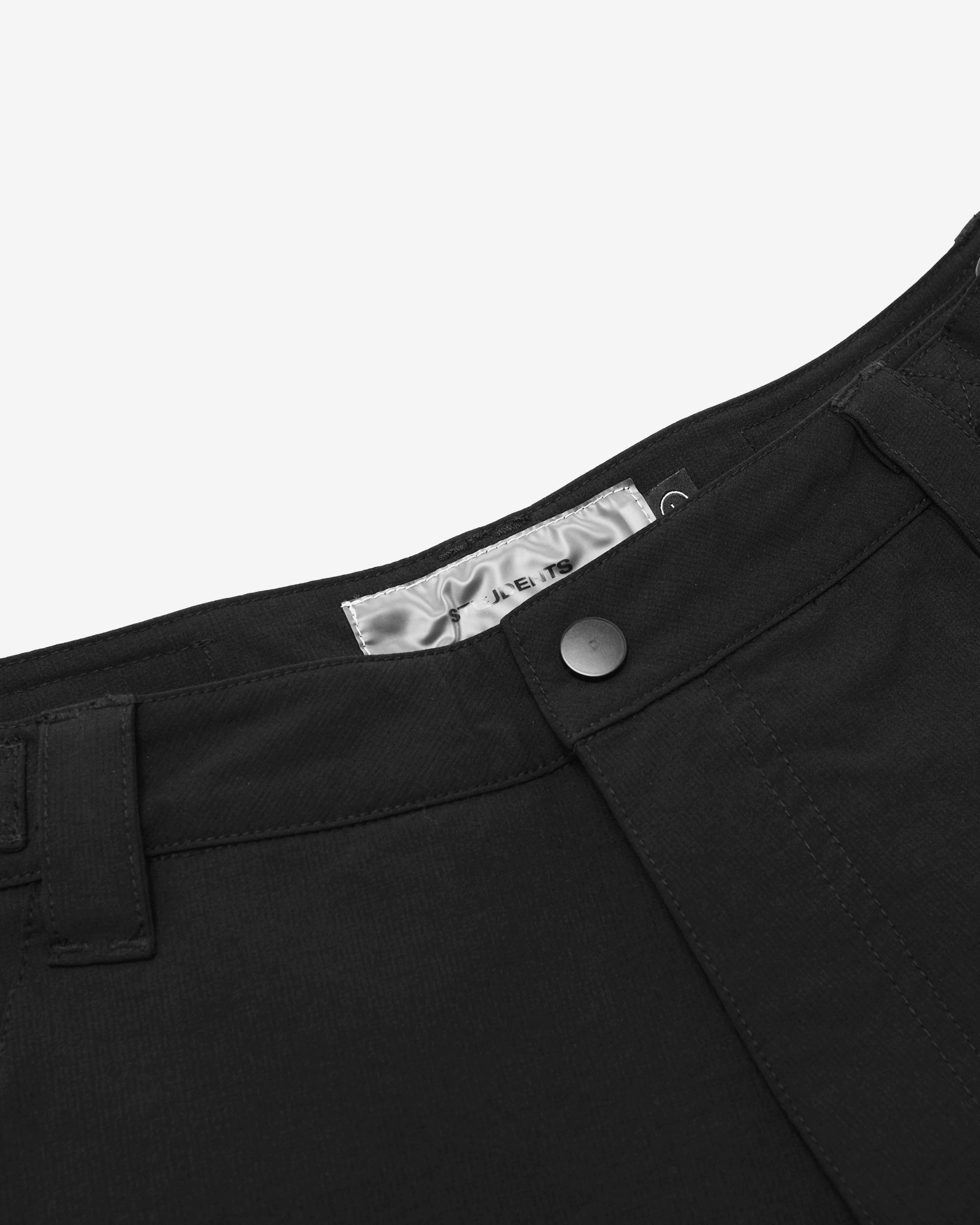 Close-up of black pants with a button and label on a white background