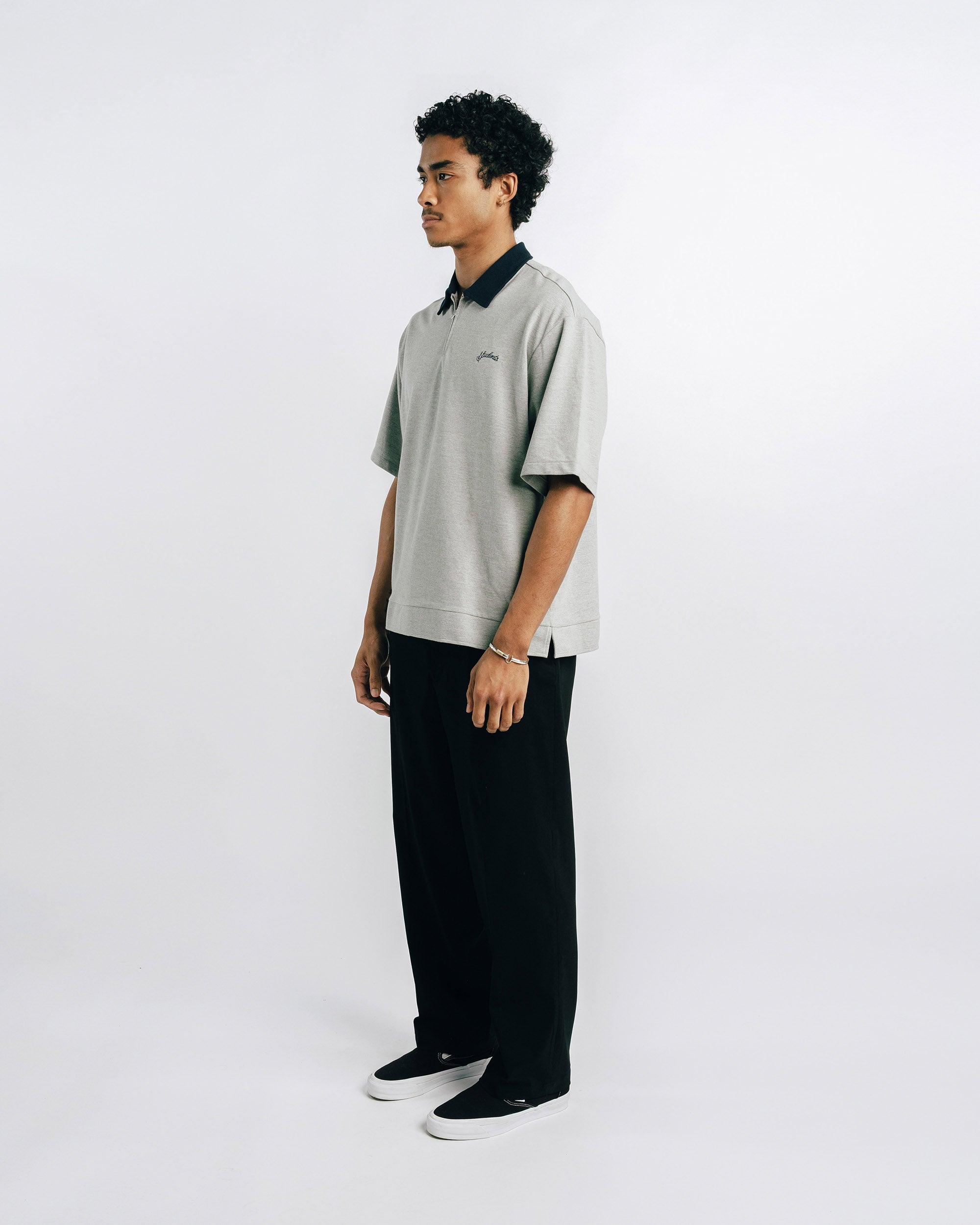 Person wearing a light gray polo shirt with black collar and trim, standing against a white background