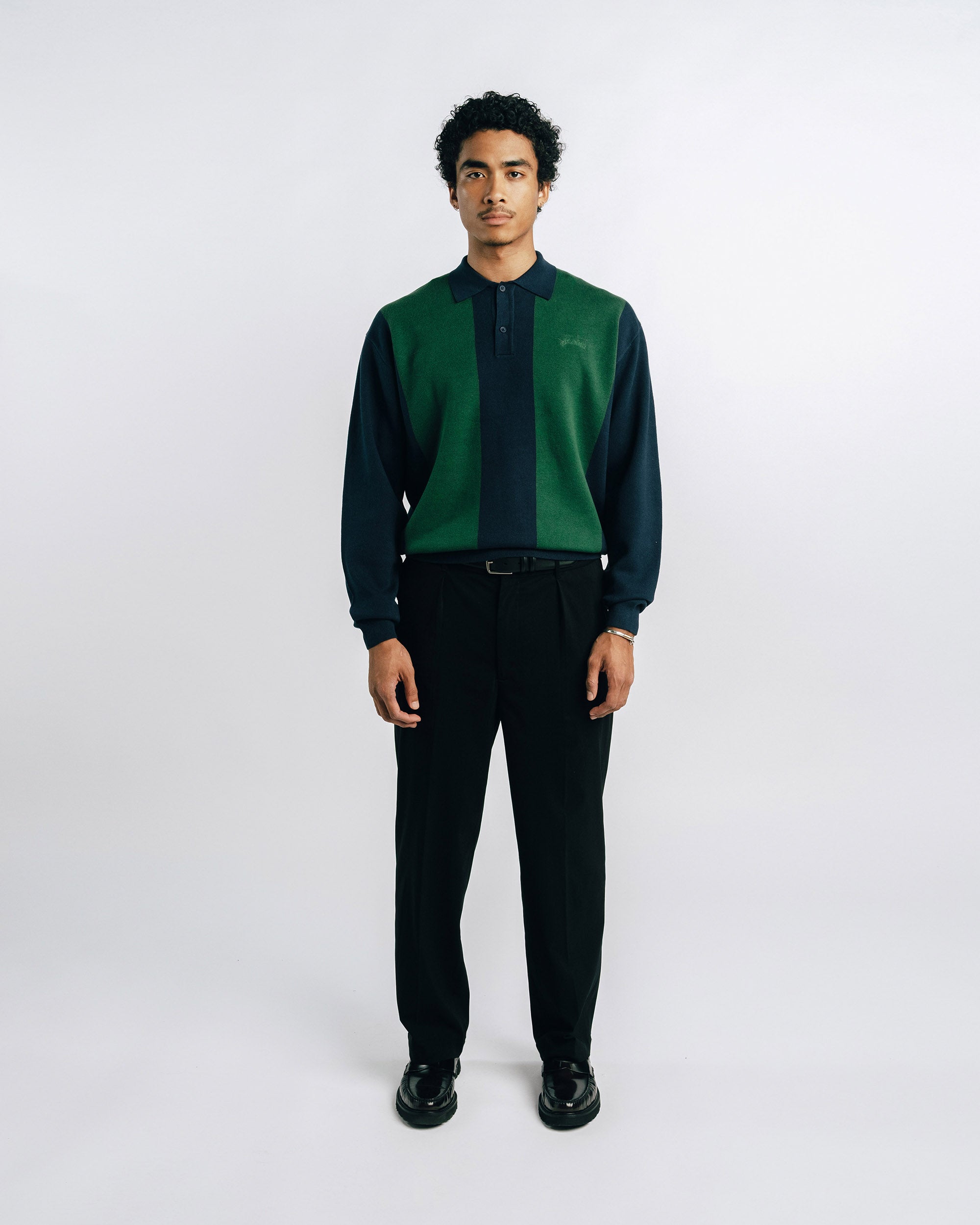 Man wearing a green and black shirt with black pants on a white background