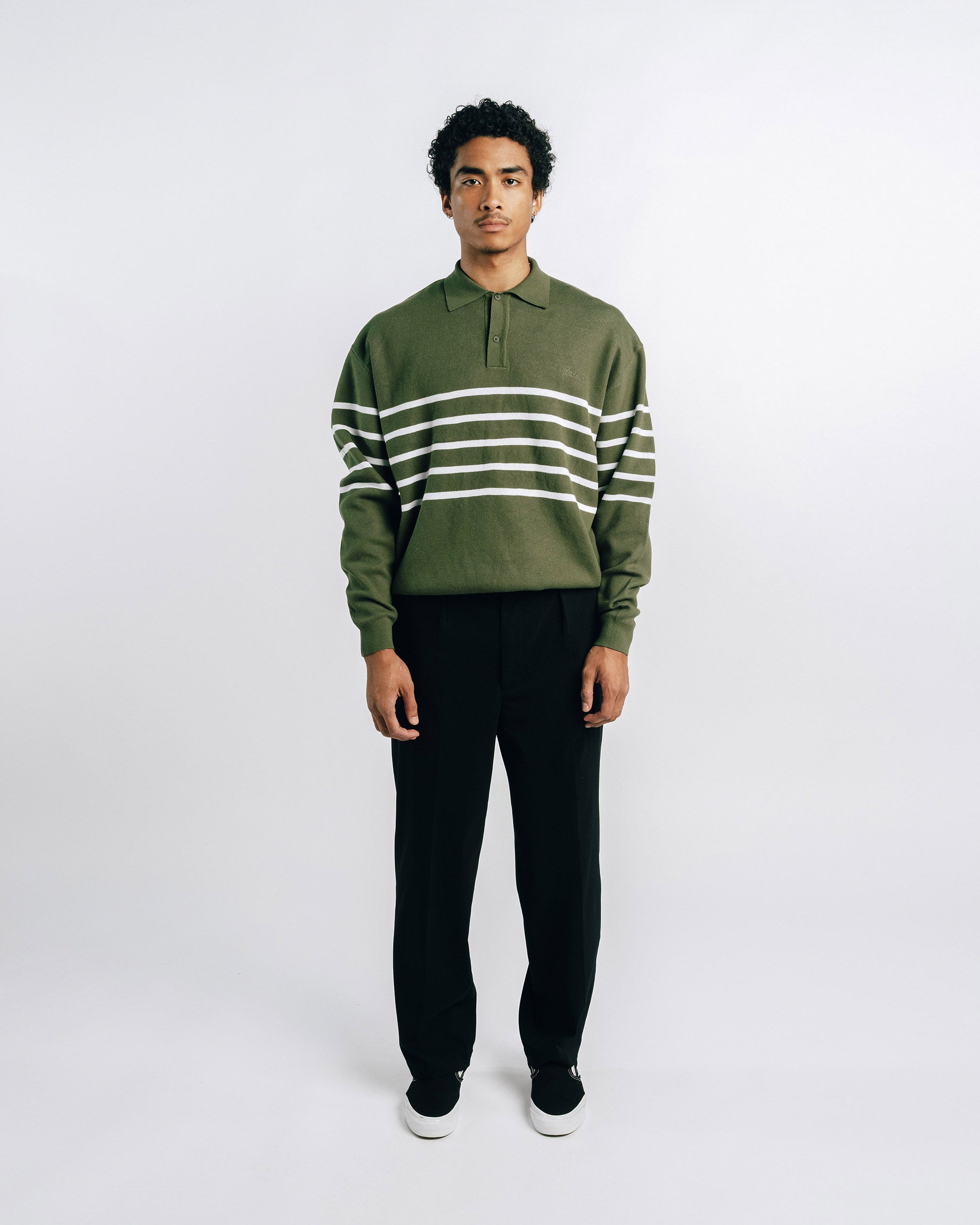 Person wearing a green and white striped sweater with black pants on a white background