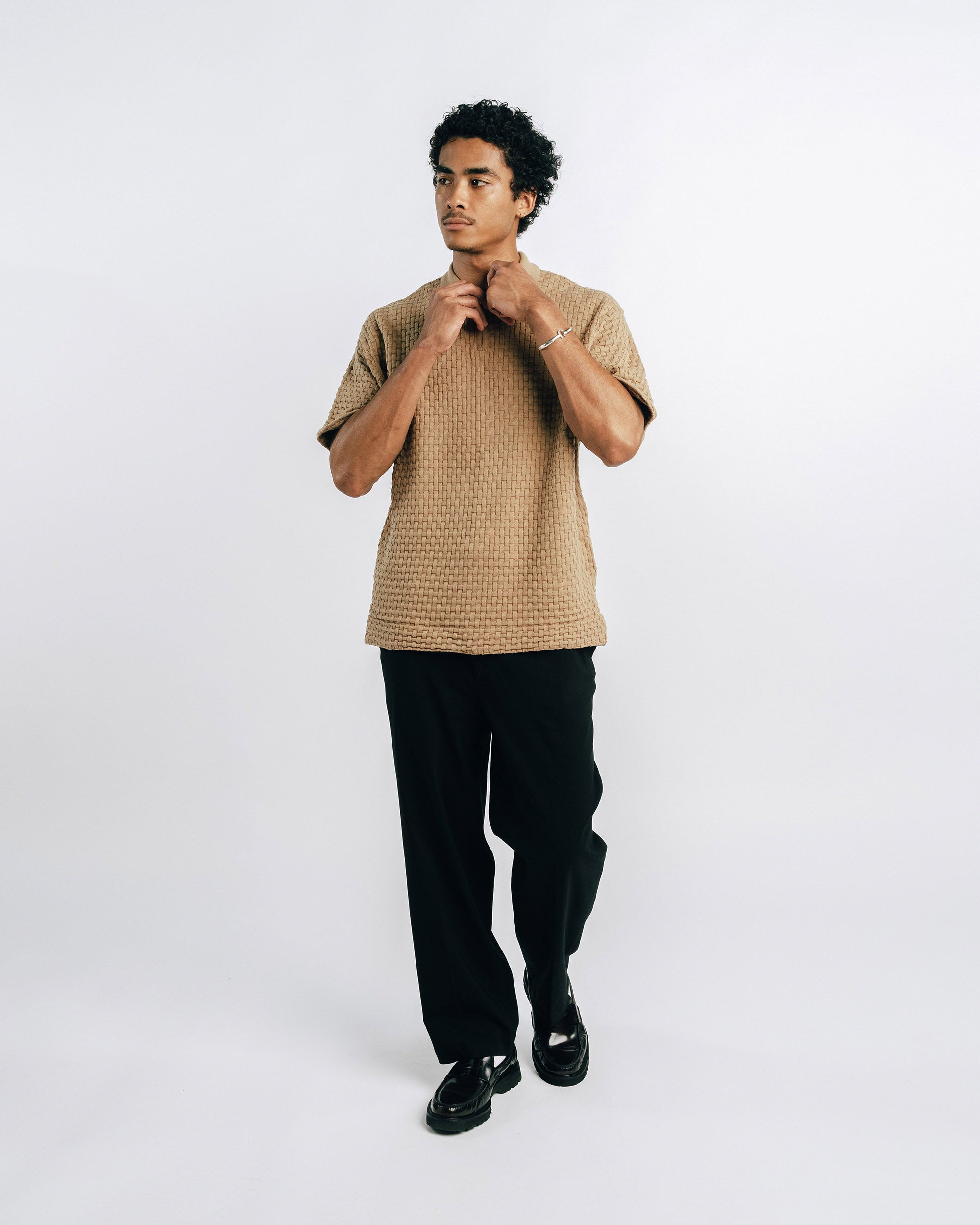 Man wearing a brown textured shirt and black pants on a white background