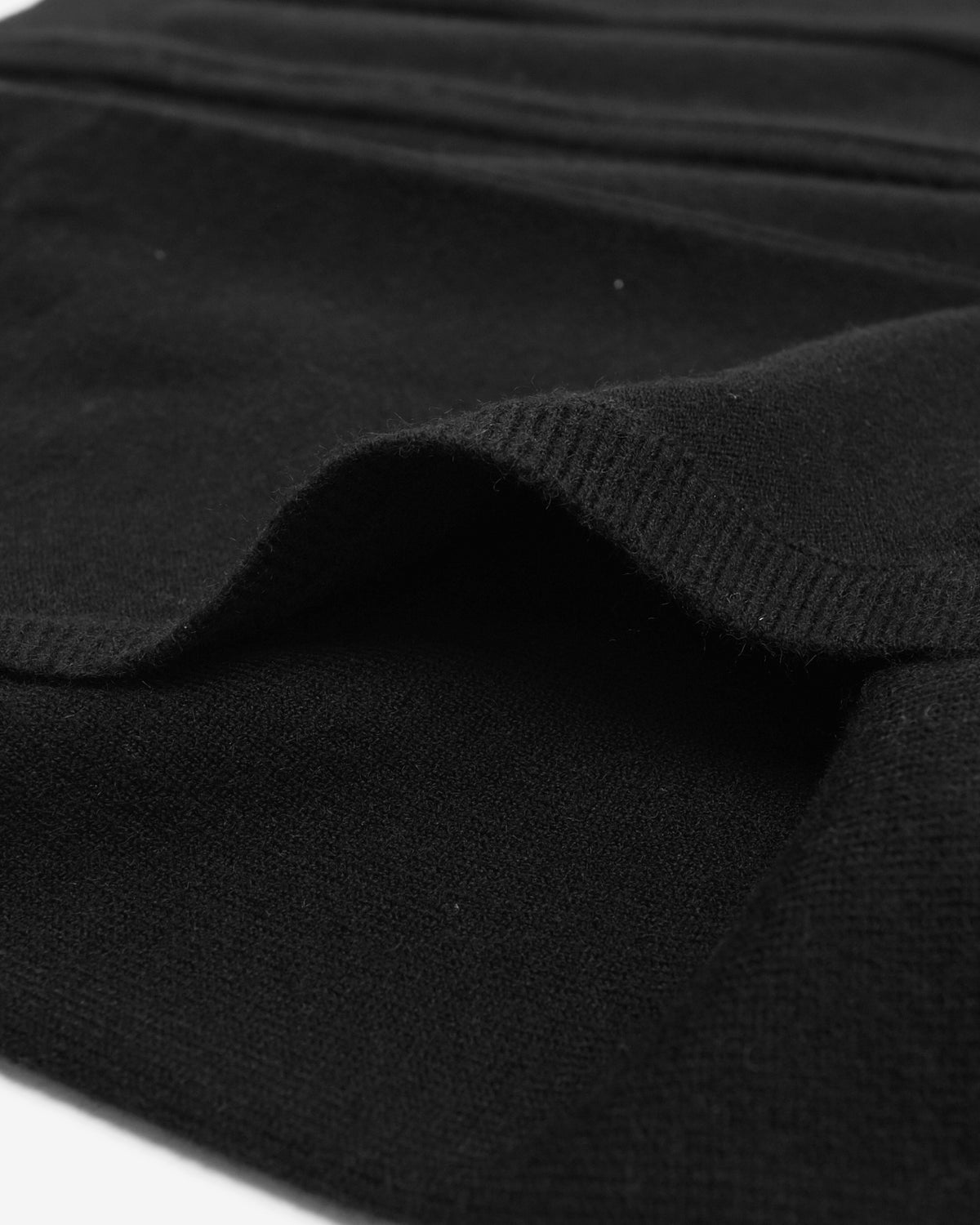 Close-up of a black ribbed knit fabric, showing the texture and folded edges of the material.