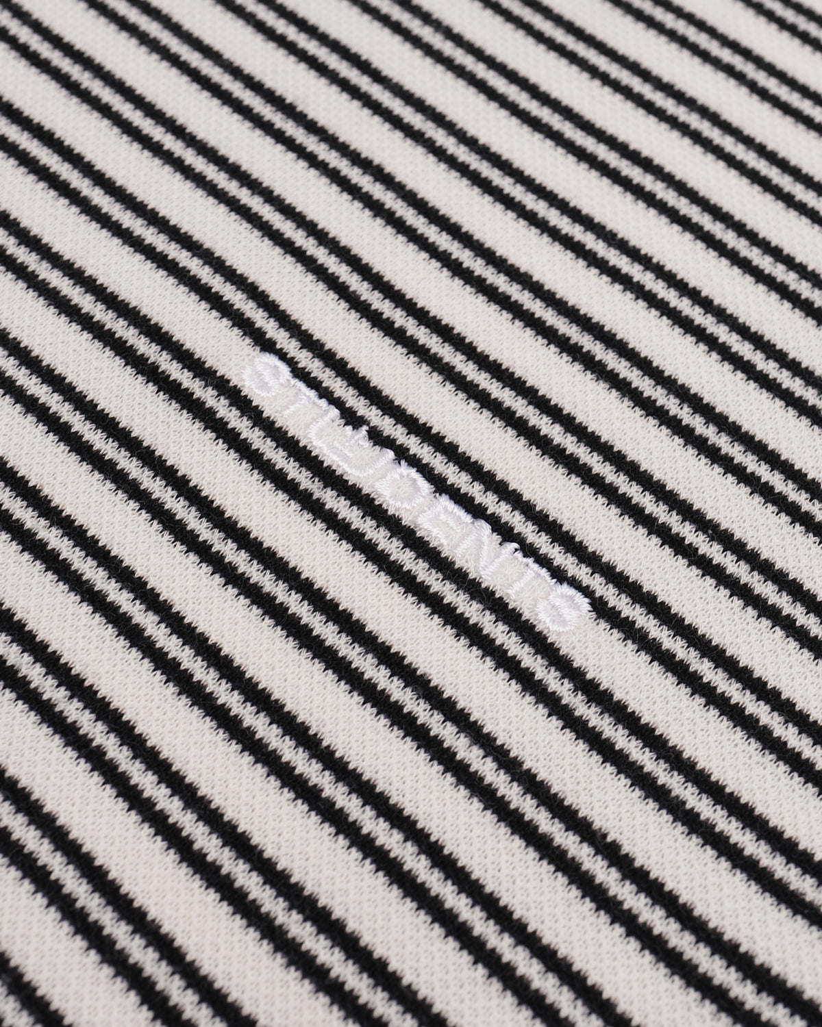 Close-up of a black and off-white striped knit fabric with a subtle diagonal watermark.