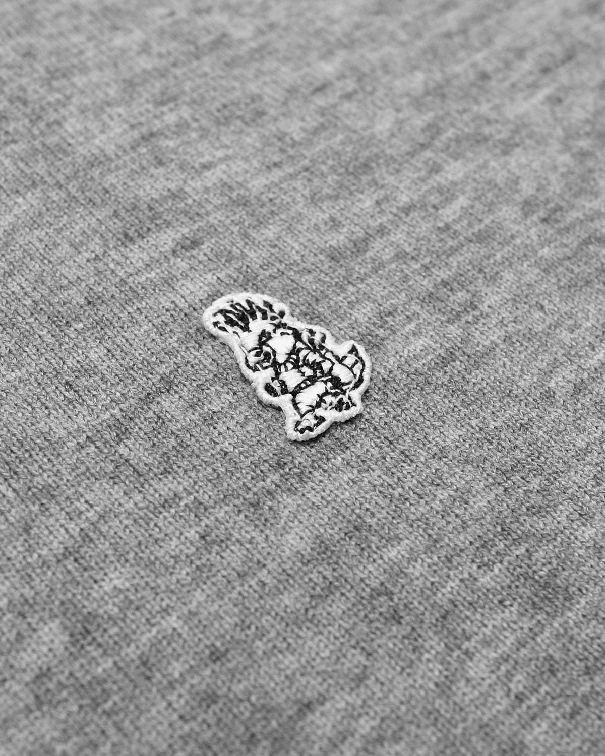 Close-up of a gray heather knit fabric with a small embroidered white bunny patch outlined in black.