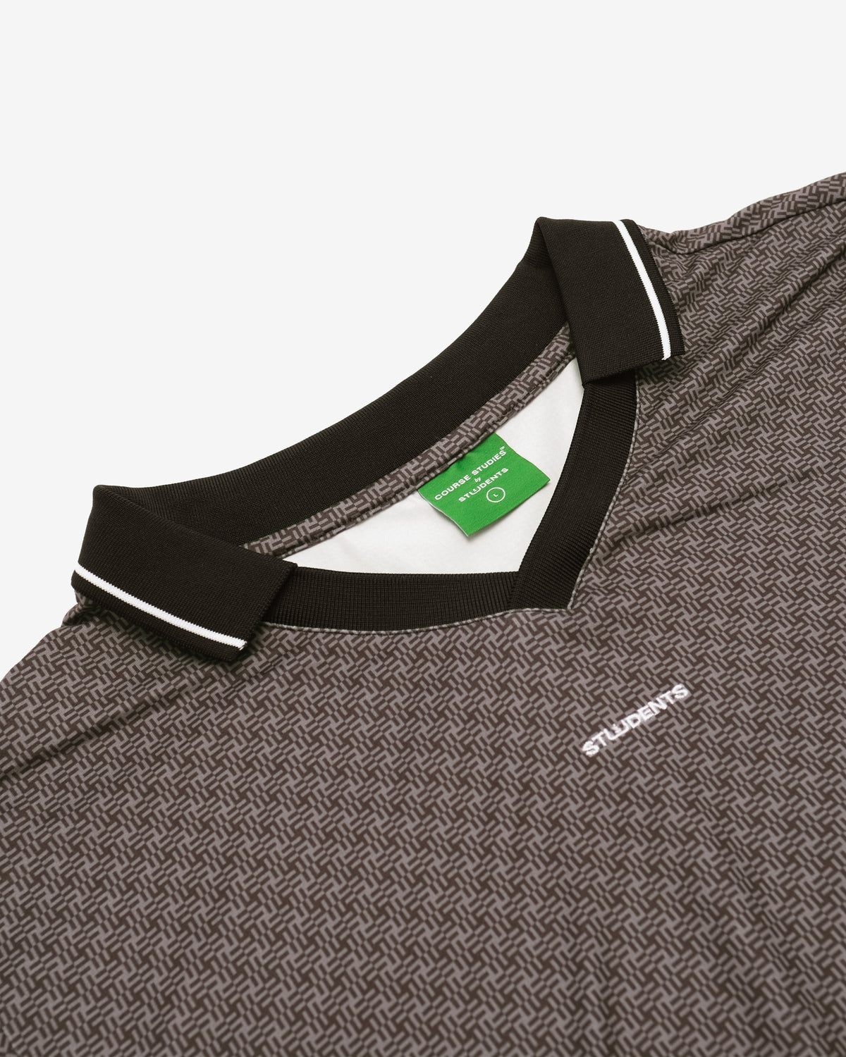 Close-up of a dark gray and black patterned polo shirt with a black collar featuring white piping, a green neck label, and a small white embroidered logo on the chest.