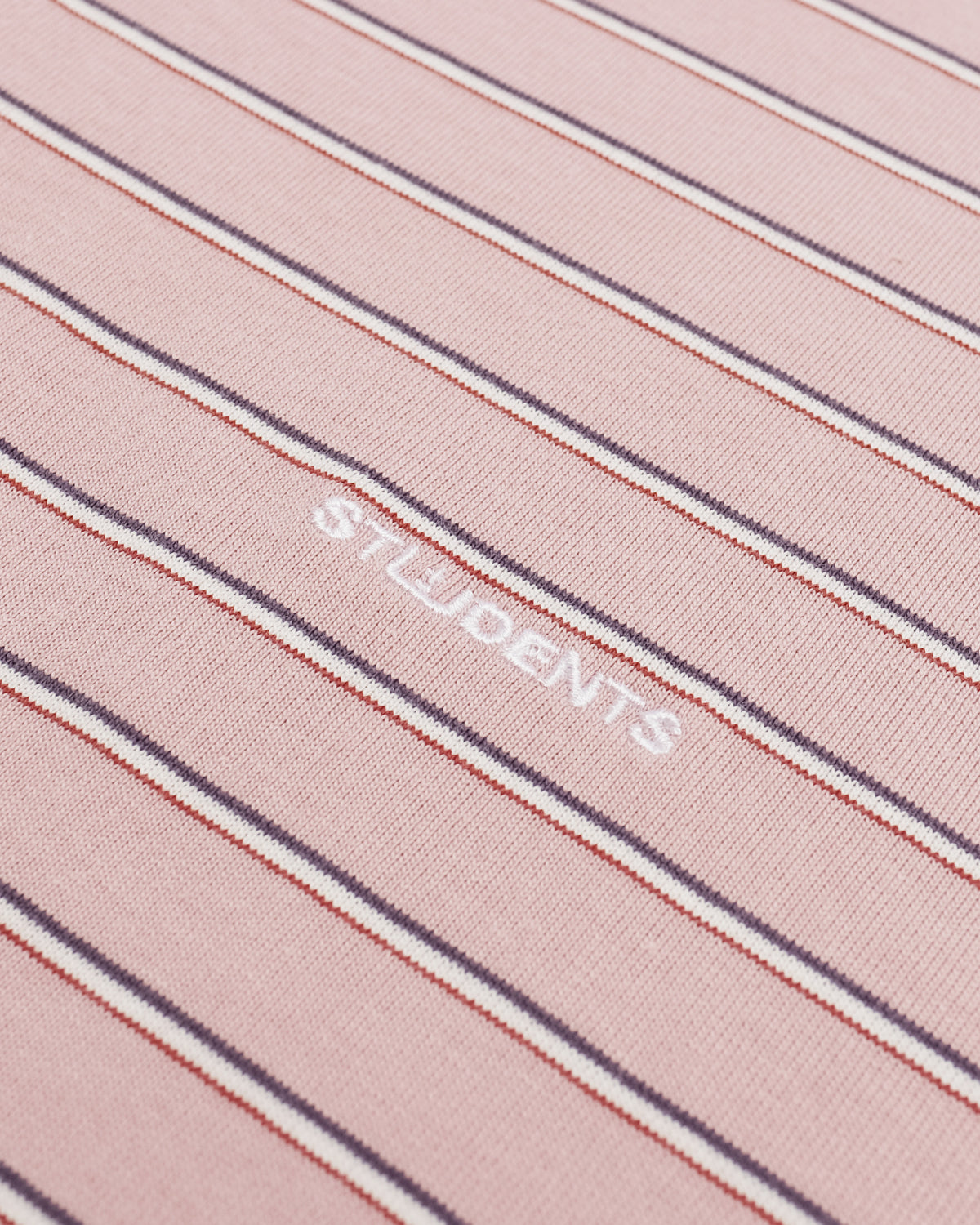 A close-up of a pink knit fabric with thin vertical stripes in white, navy, and red, featuring the word 'STUDENTS' woven in white across the center.