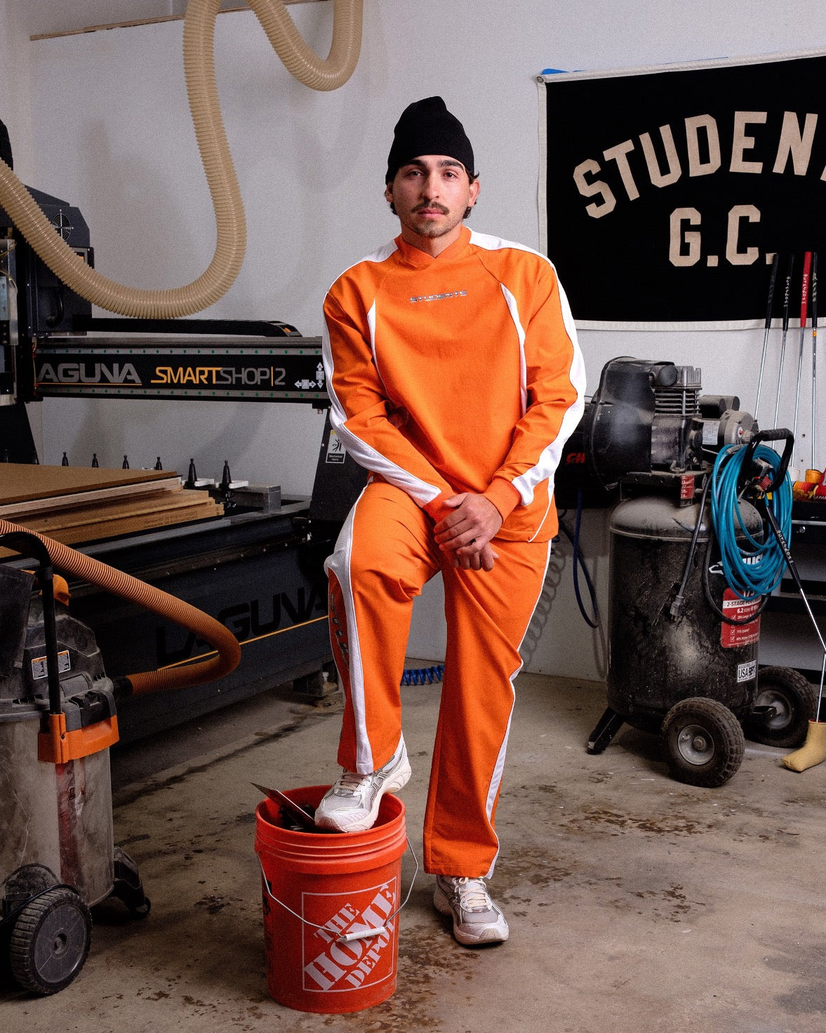 Person in orange jumpsuit standing in a workshop with tools and equipment.