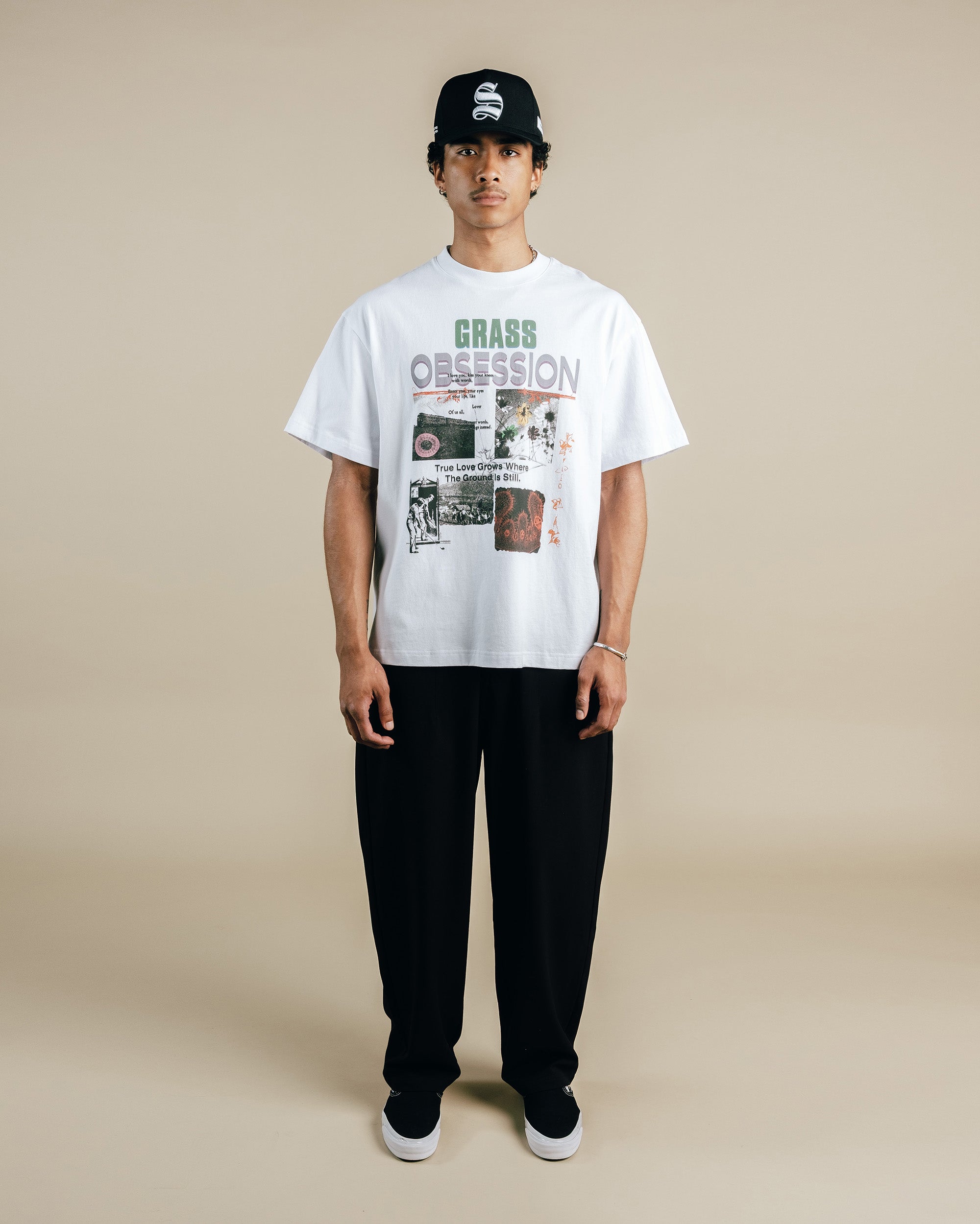 Person wearing a white t-shirt with graphic design and black pants on a beige background