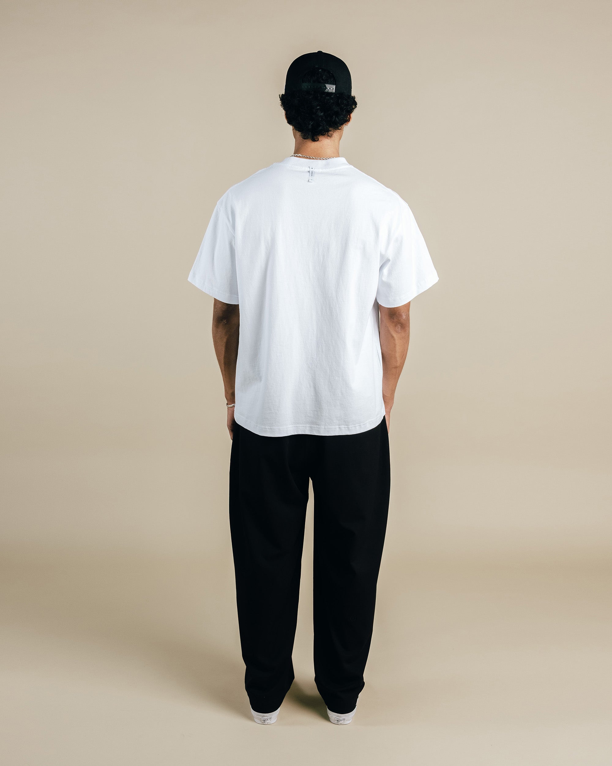 Person wearing a white t-shirt and black pants on a beige background