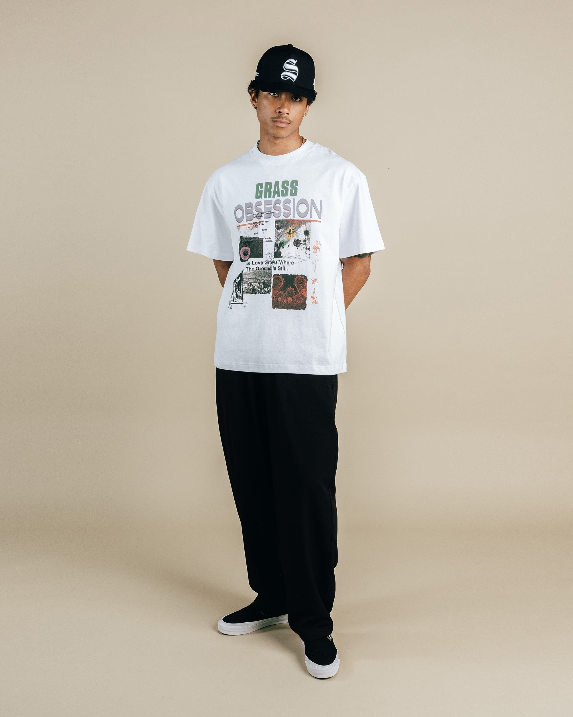 Person wearing a white graphic t-shirt and black pants on a beige background