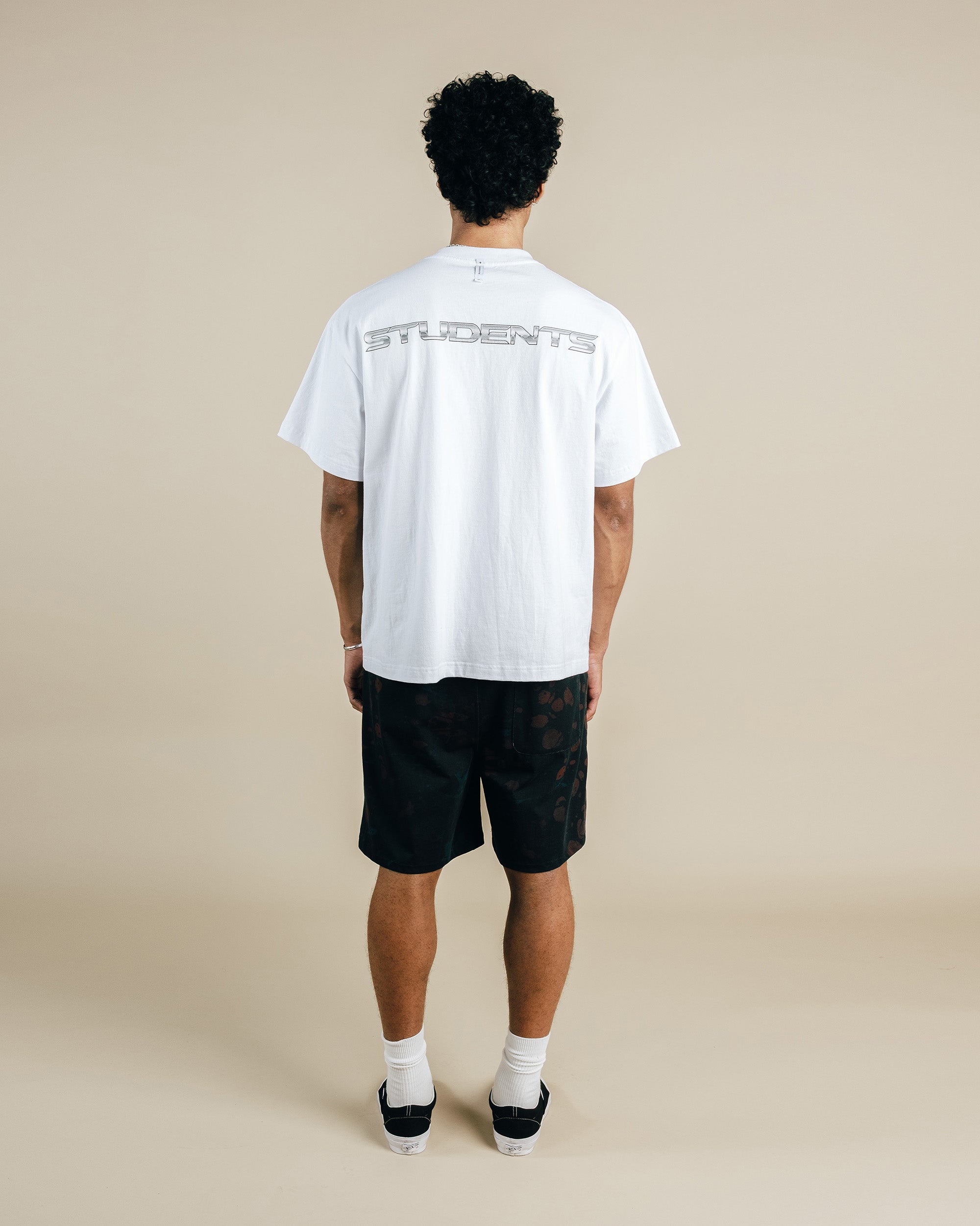 Person wearing a white t-shirt with text on the back and black shorts against a beige background