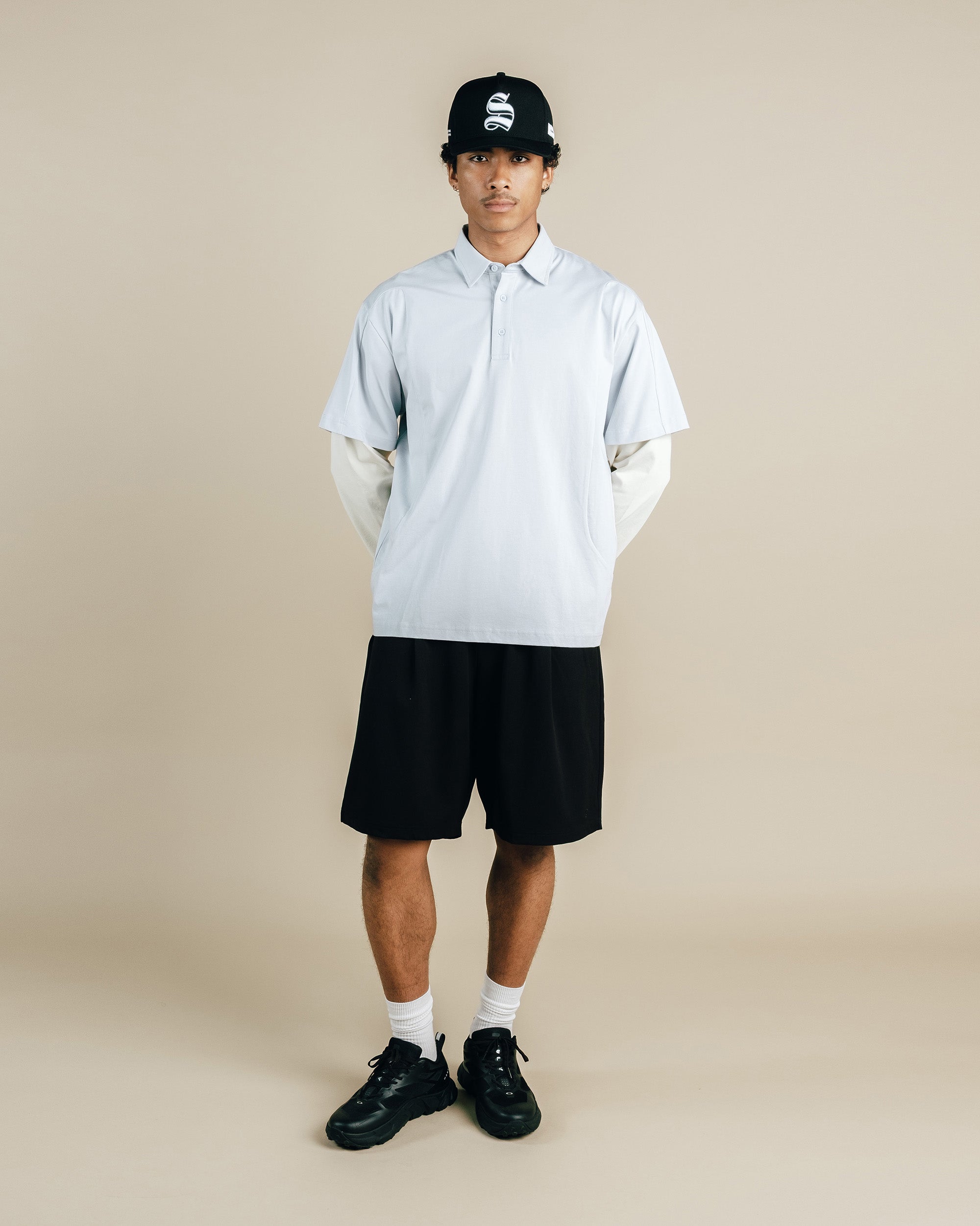 Person wearing a light blue shirt, black shorts, and black shoes on a beige background
