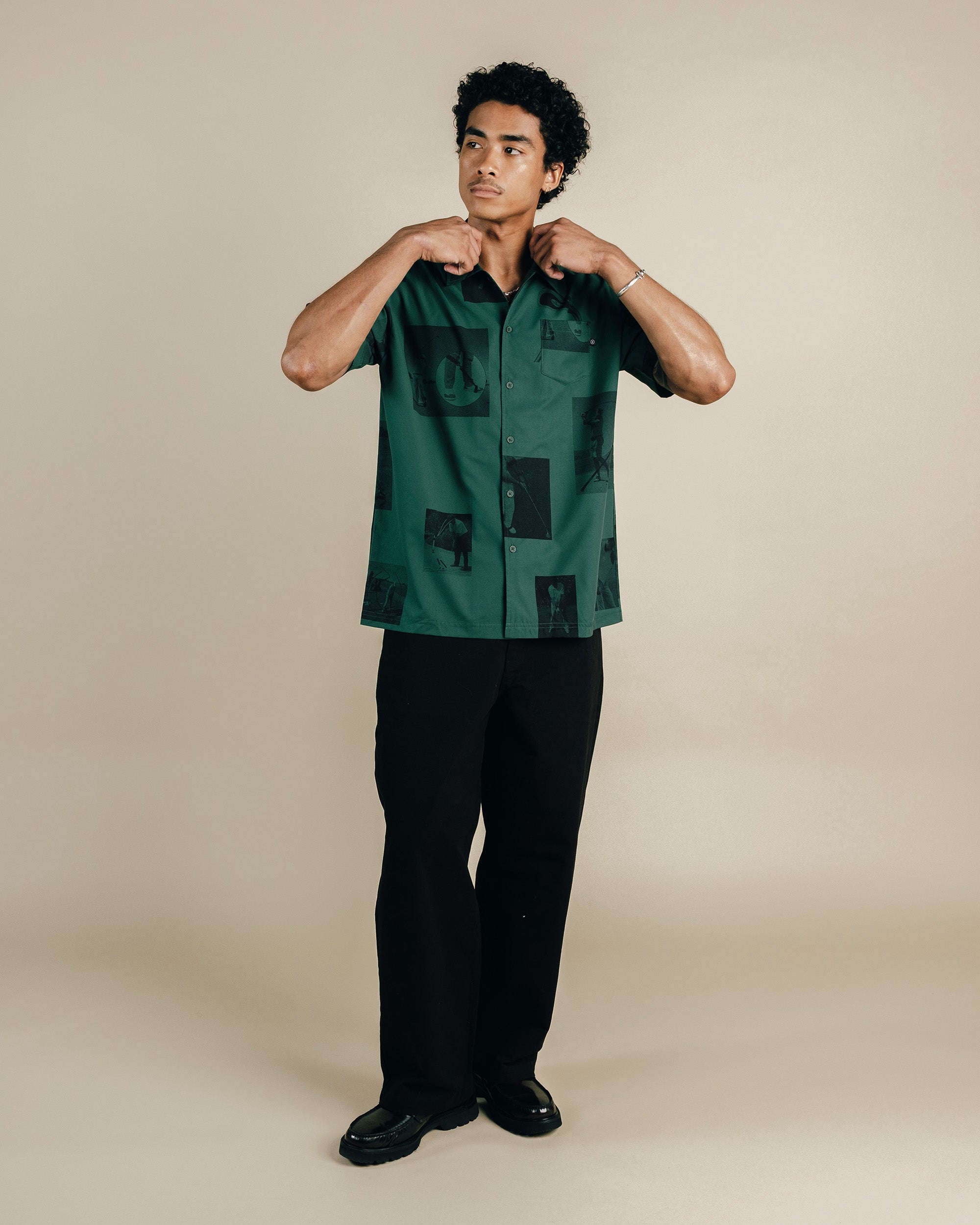 Man wearing a green patterned shirt and black pants on a beige background