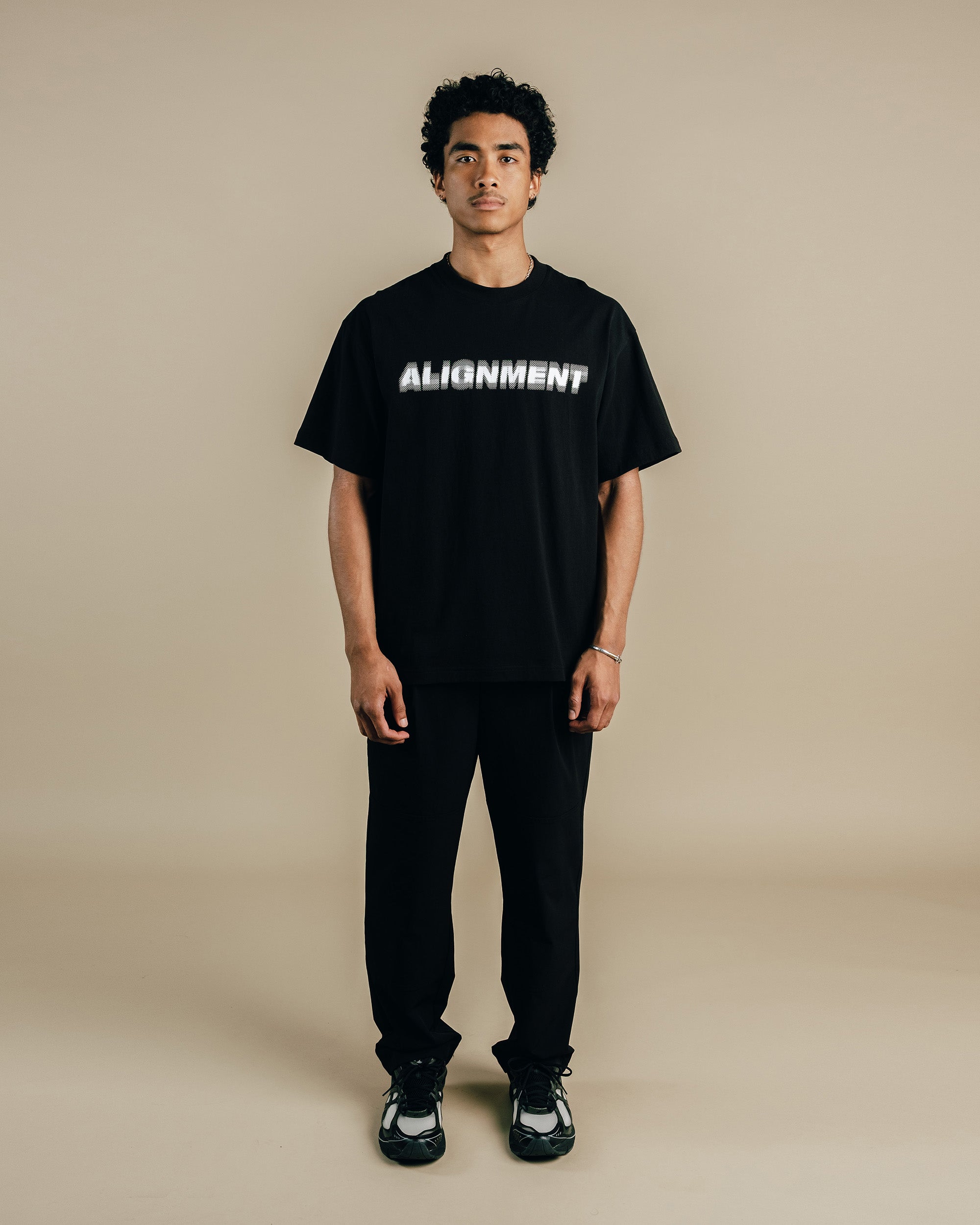 Person wearing a black t-shirt with 'ALIGNMENT' text on a beige background